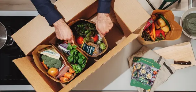 Fresh vegetables and groceries being unpacked from a food box in a home kitchen