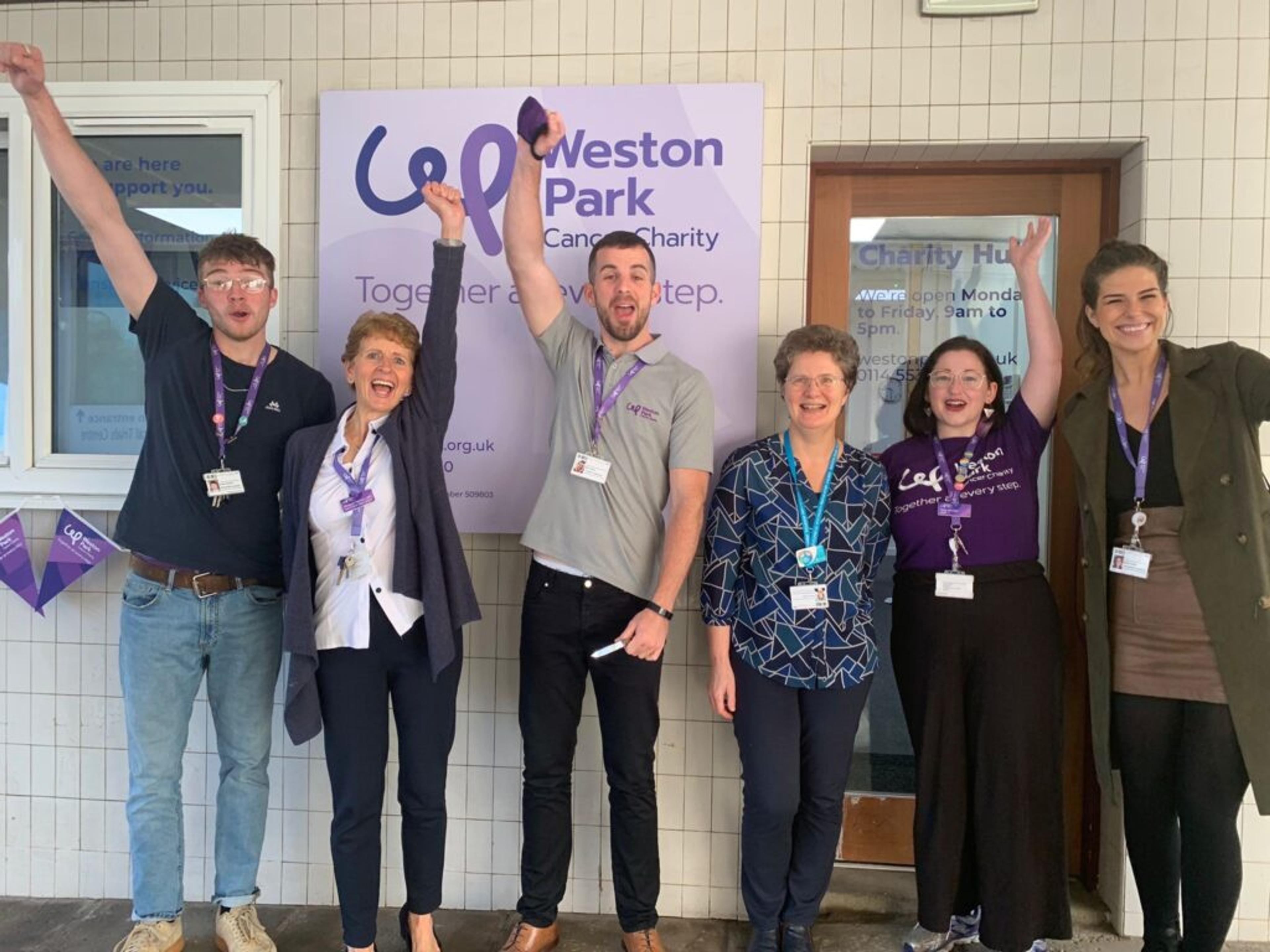 Six members of Weston Park Cancer Charity stood outside an office smiling with their hands in the air.