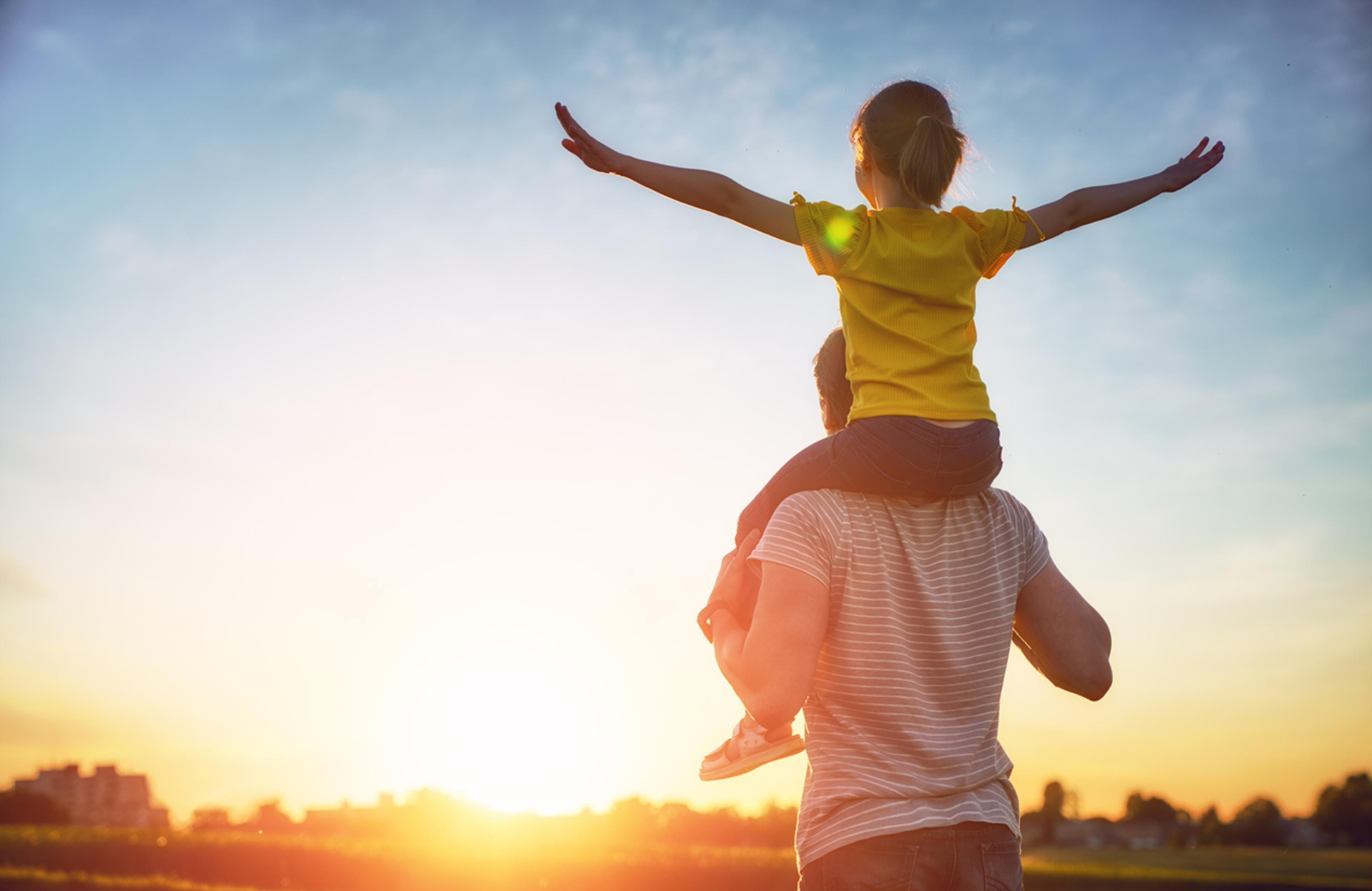 A dad with a young daughter on his shoulders looking into the sunset