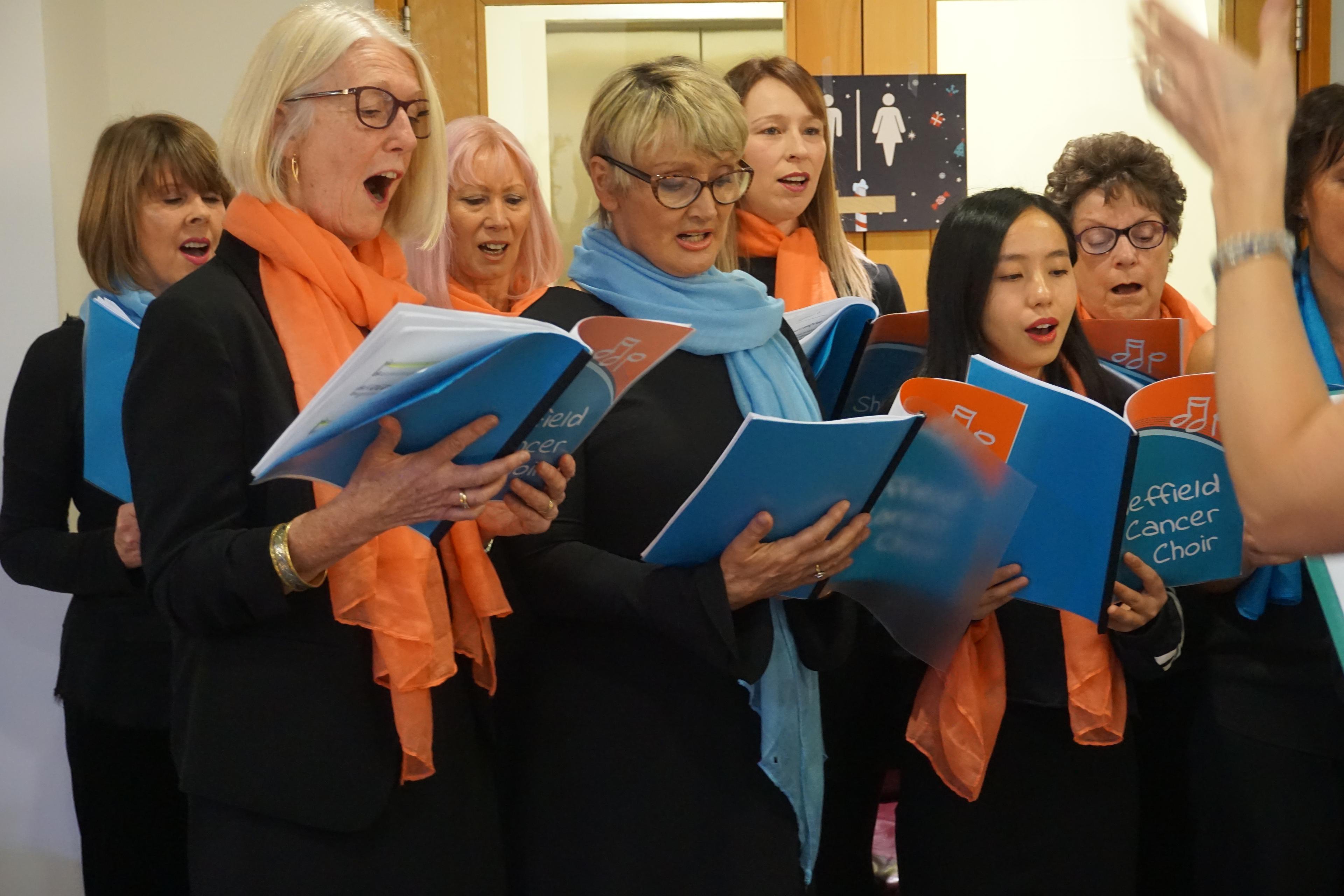 Eight members of Sheffield Cancer Choir perform indoors, holding sheets of music.