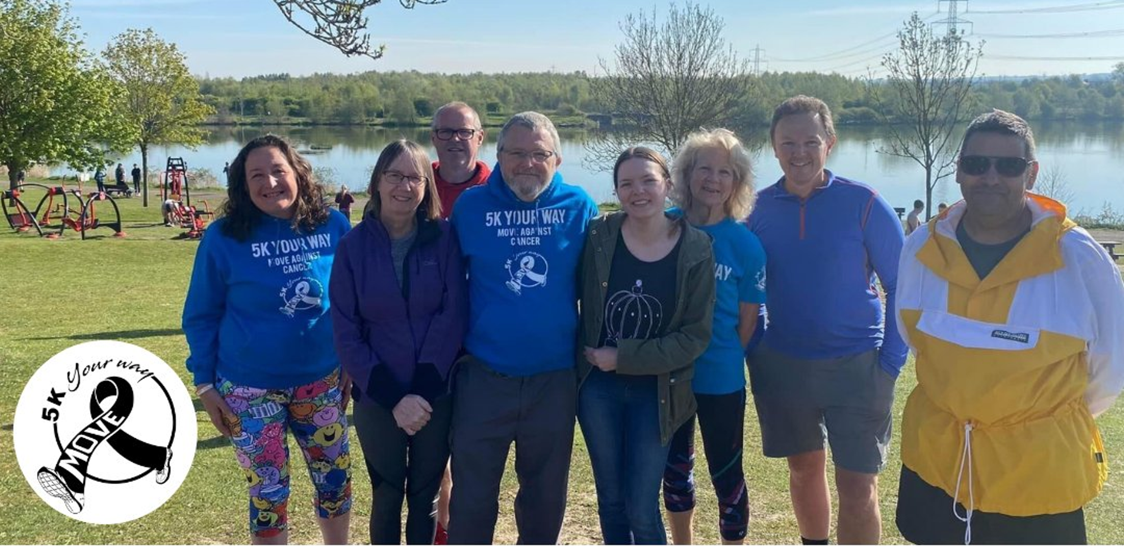 A group of people - four women and four men - stand in front of a lake just before they are due to take part in a 5k run to support cancer care and research.
