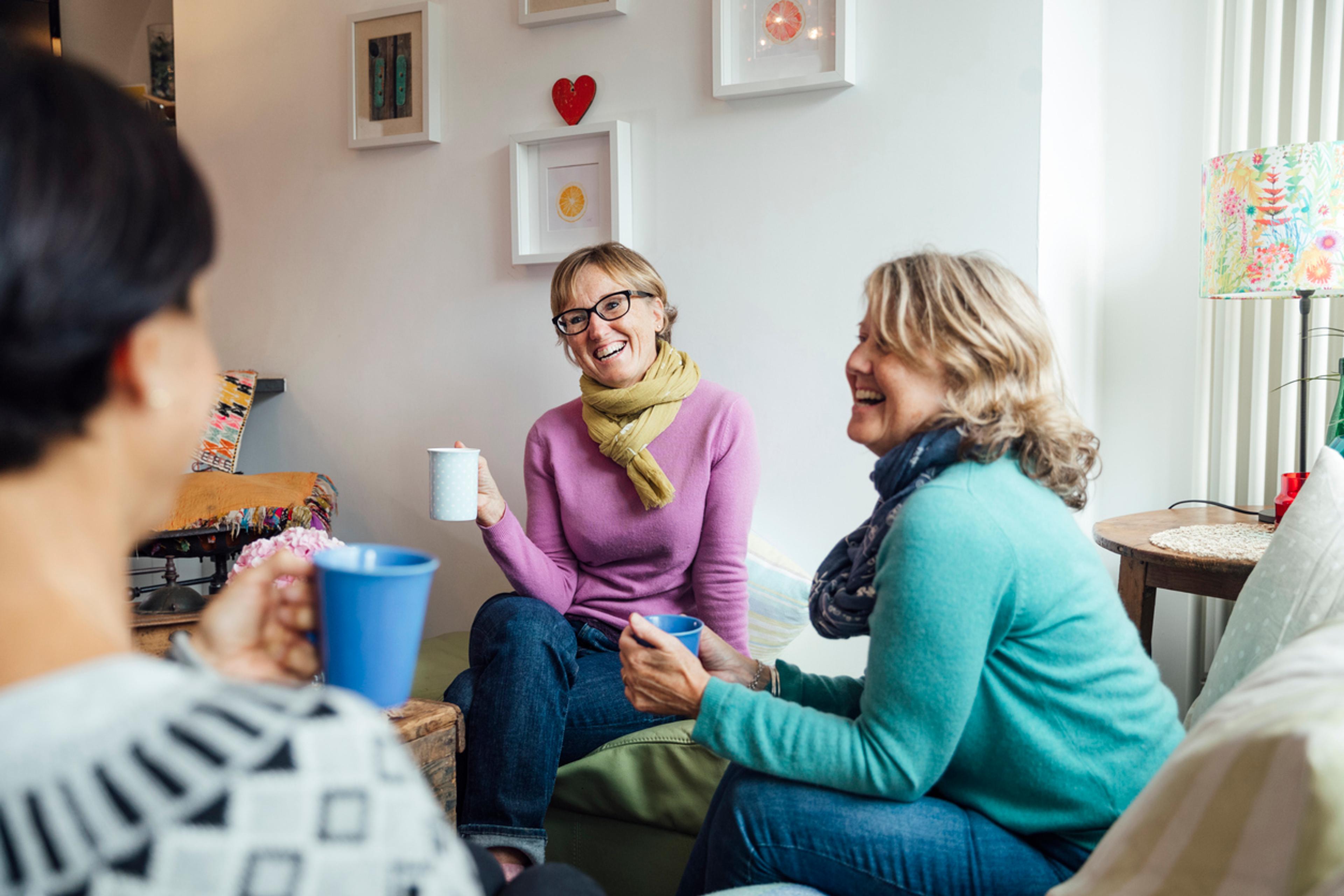 A group of women sat in a living room having cups of tea, laughing