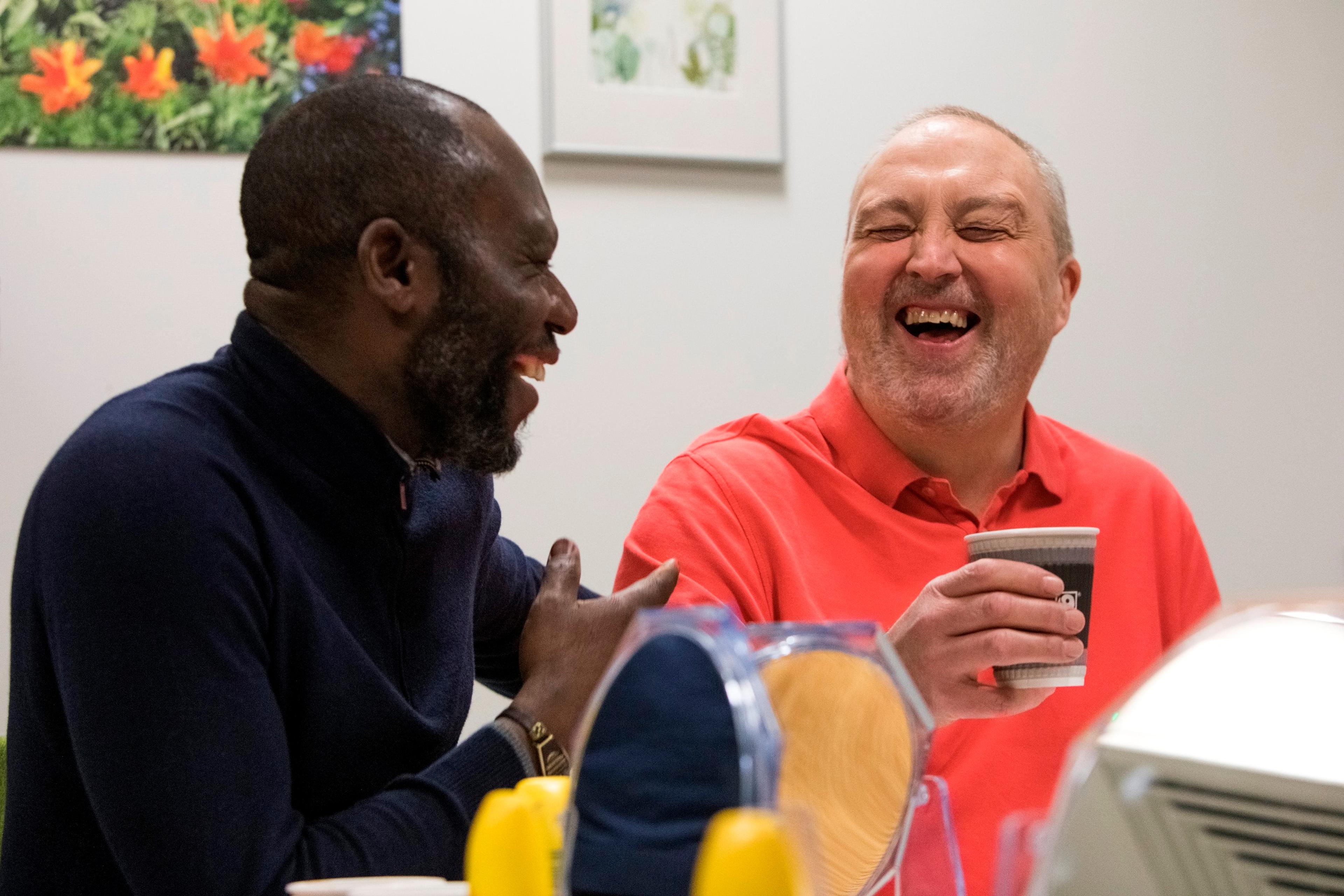 Two men having a hot drink laughing with each other