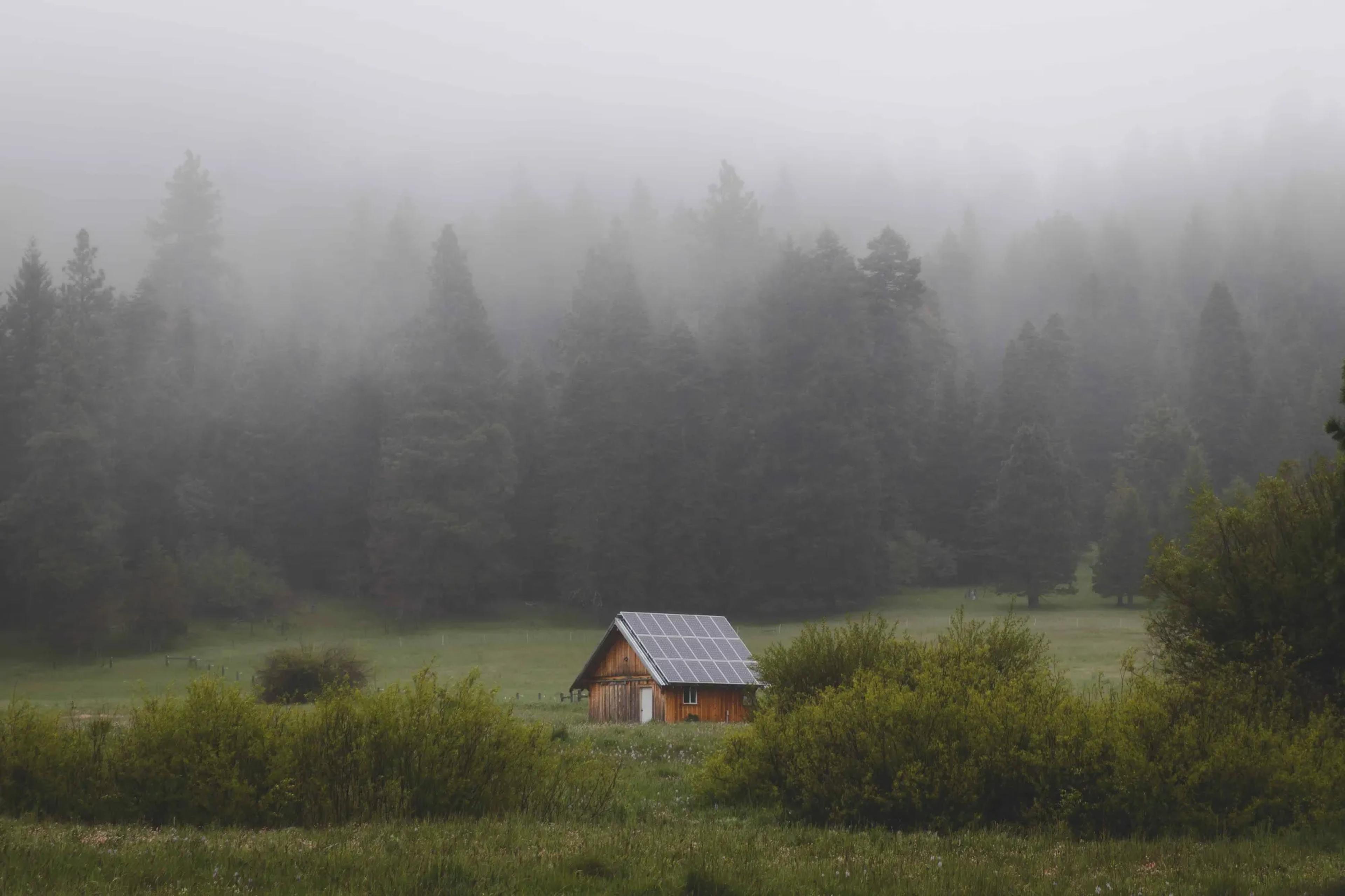 Image of a cabin in a field in the forest. The cabin has solar panels on the roof.