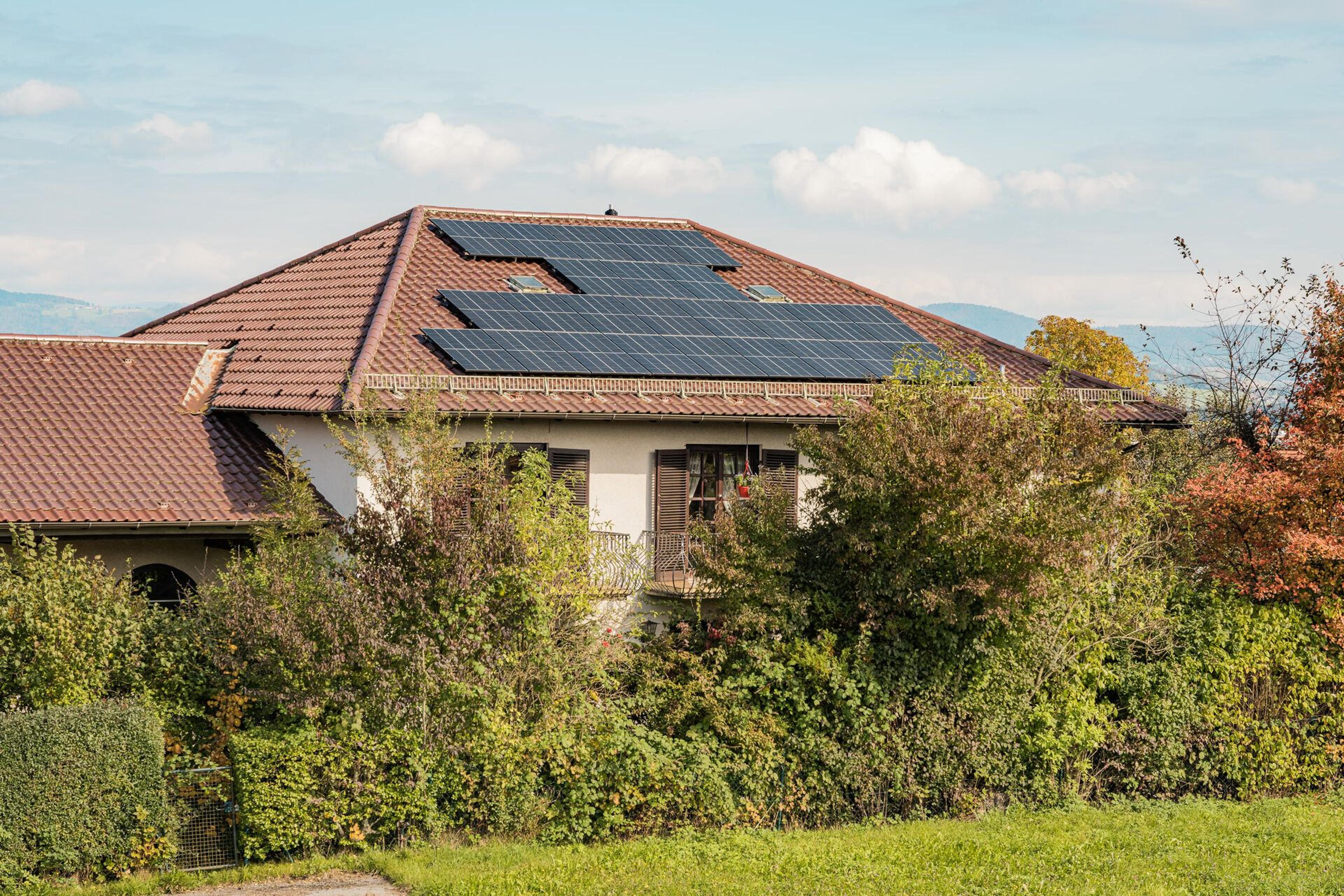 Eine Photovoltaikanlage auf einem Hausdach umgeben von grünen Pflanzen