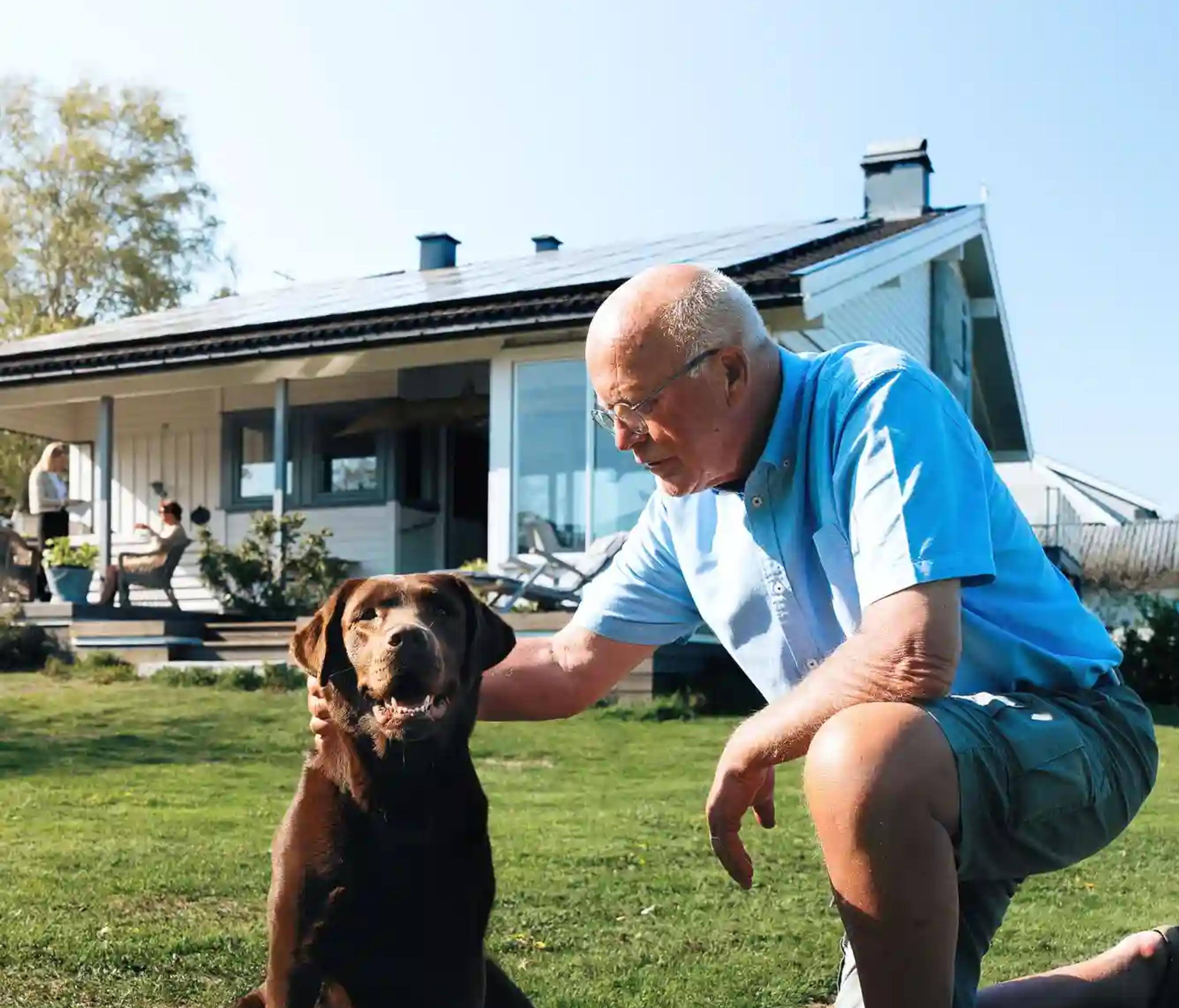 en man och sin hund framför sitt hus med solceller på taket