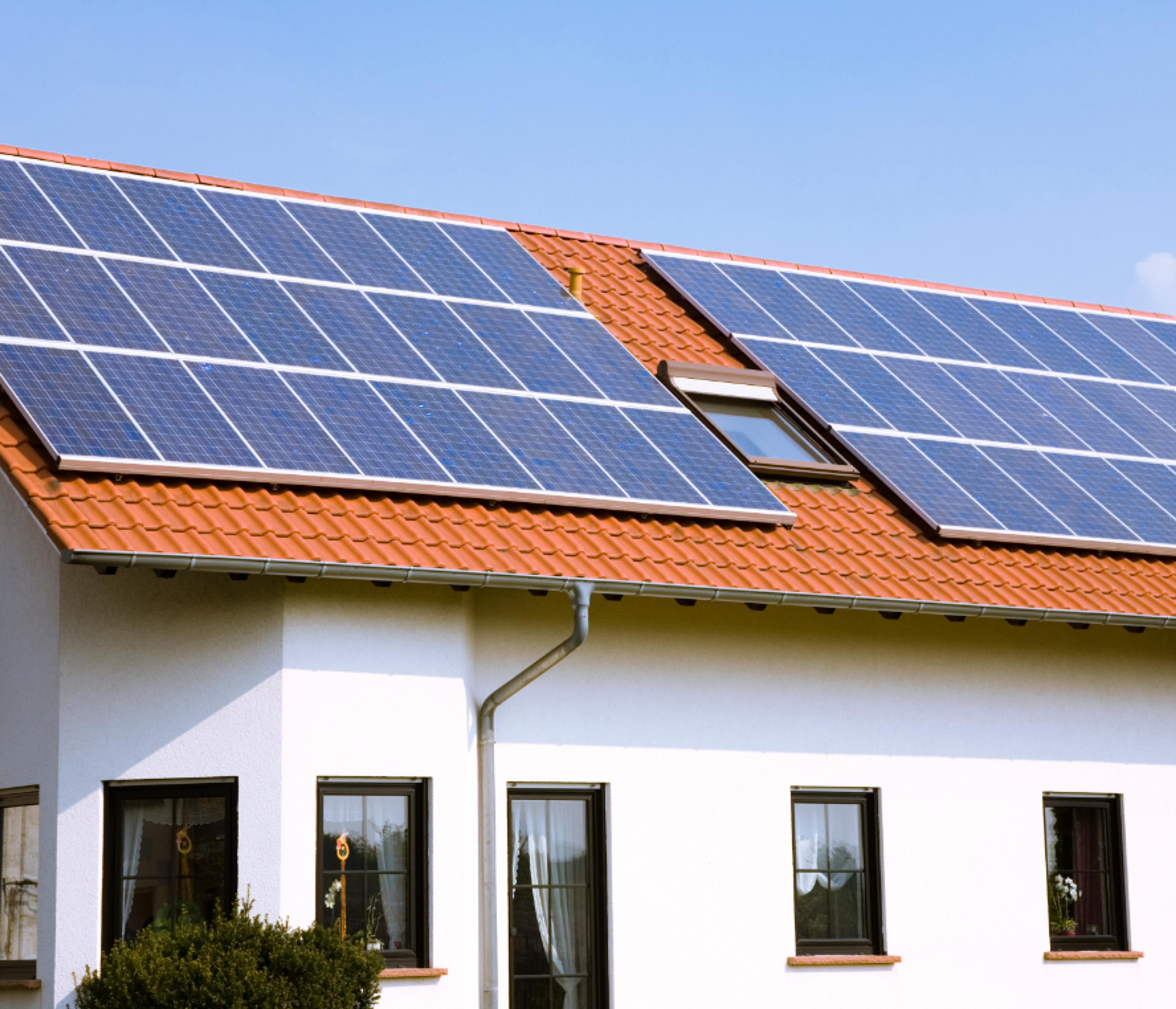 sonniges weißes Haus mit PV-Anlage auf dem Dach