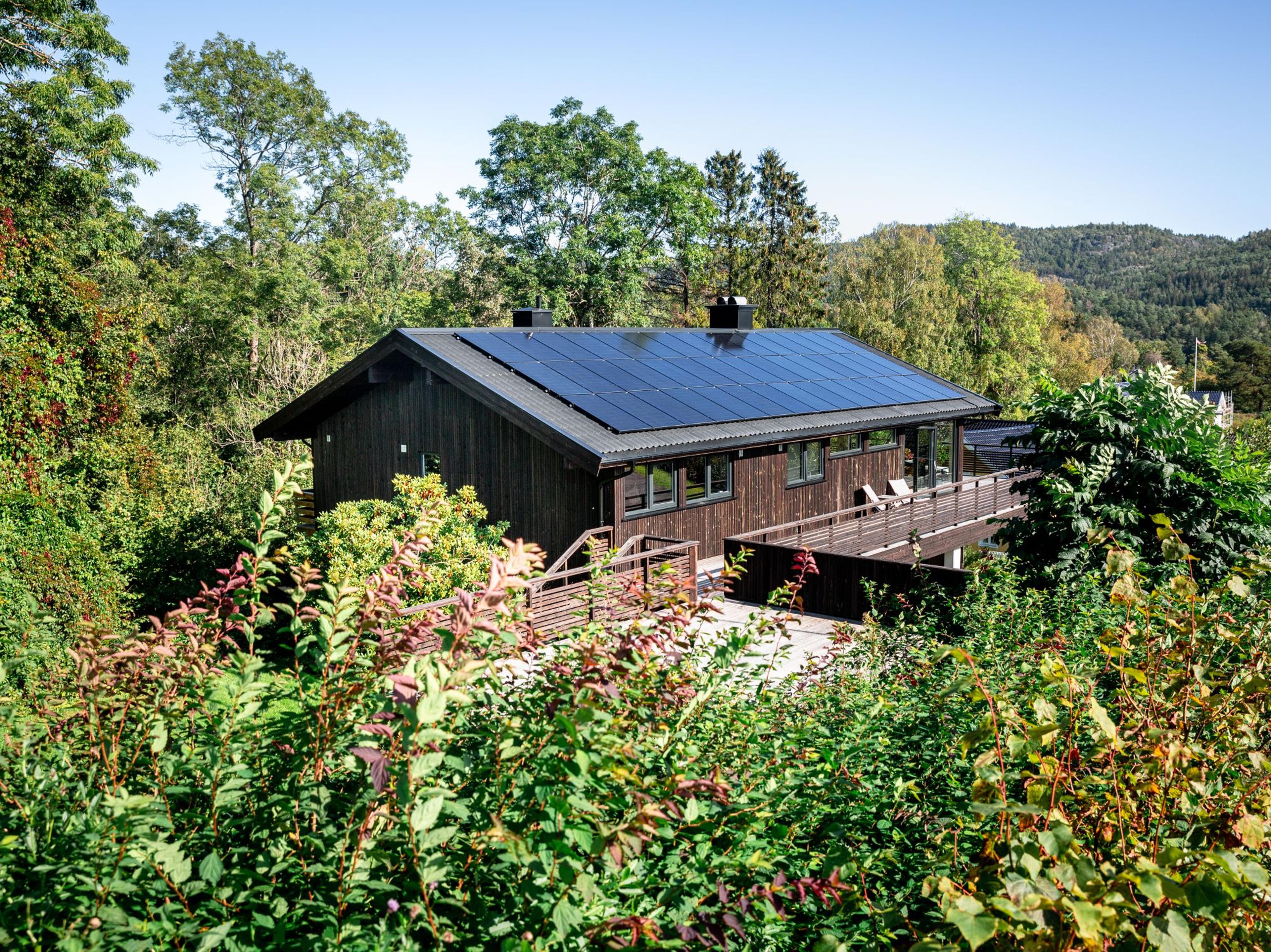 hus med installerte solcellepaneler i et frodig landskap