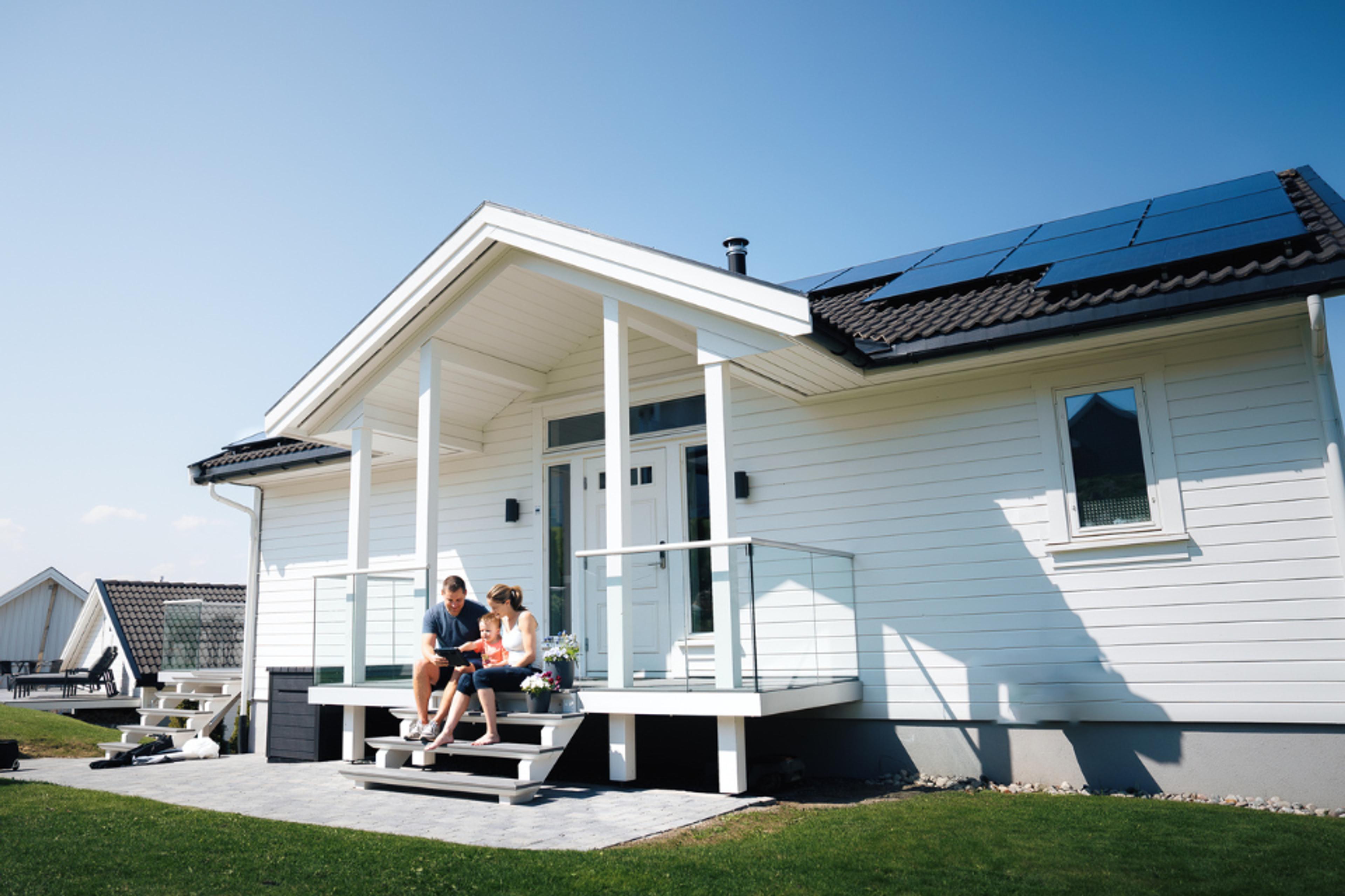 et par som sitter foran huset sitt med solcellepaneler på taket