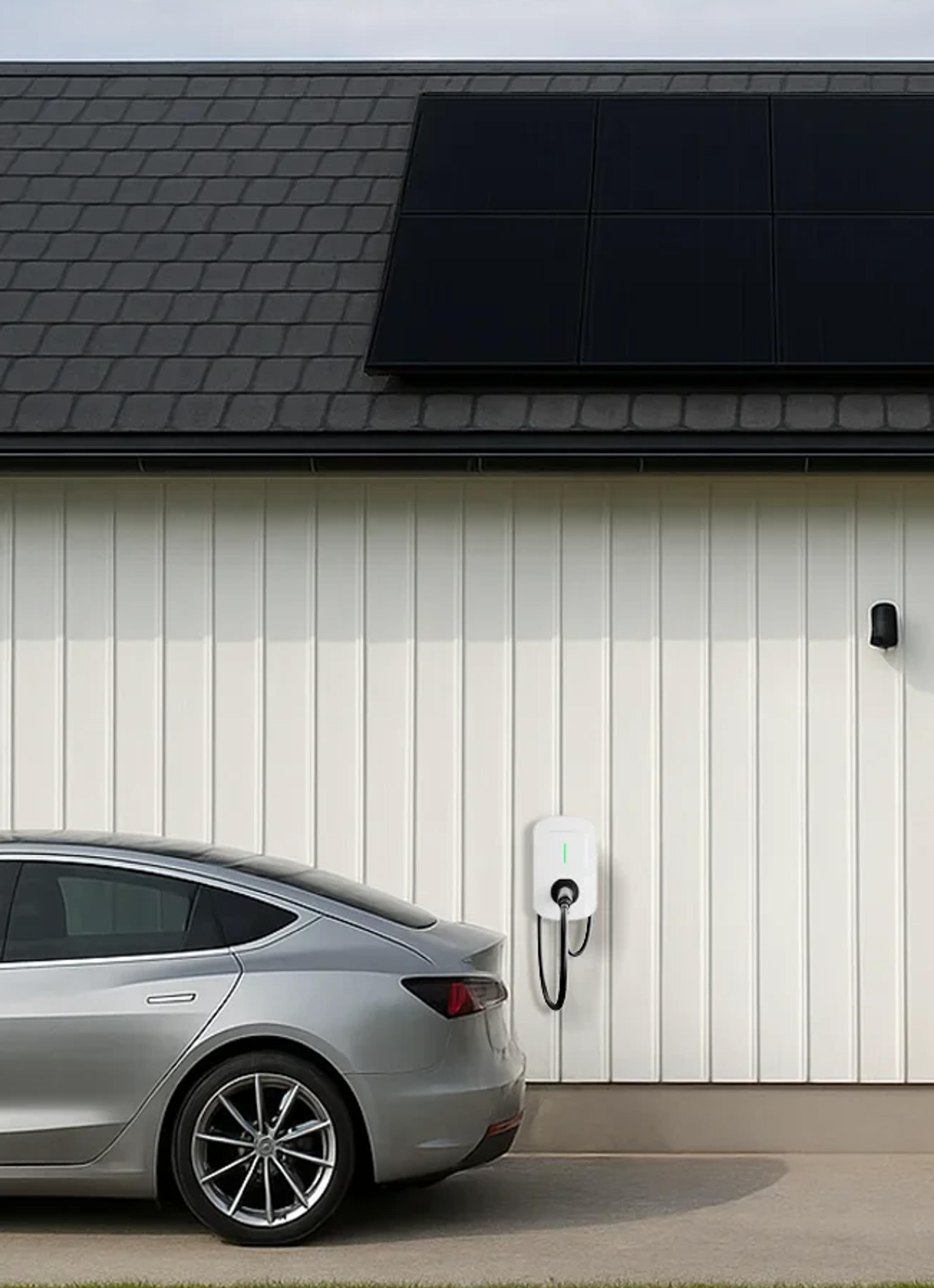 En bil lader fra en ladeboks montert på ytterveggen på et hus med solceller på taket