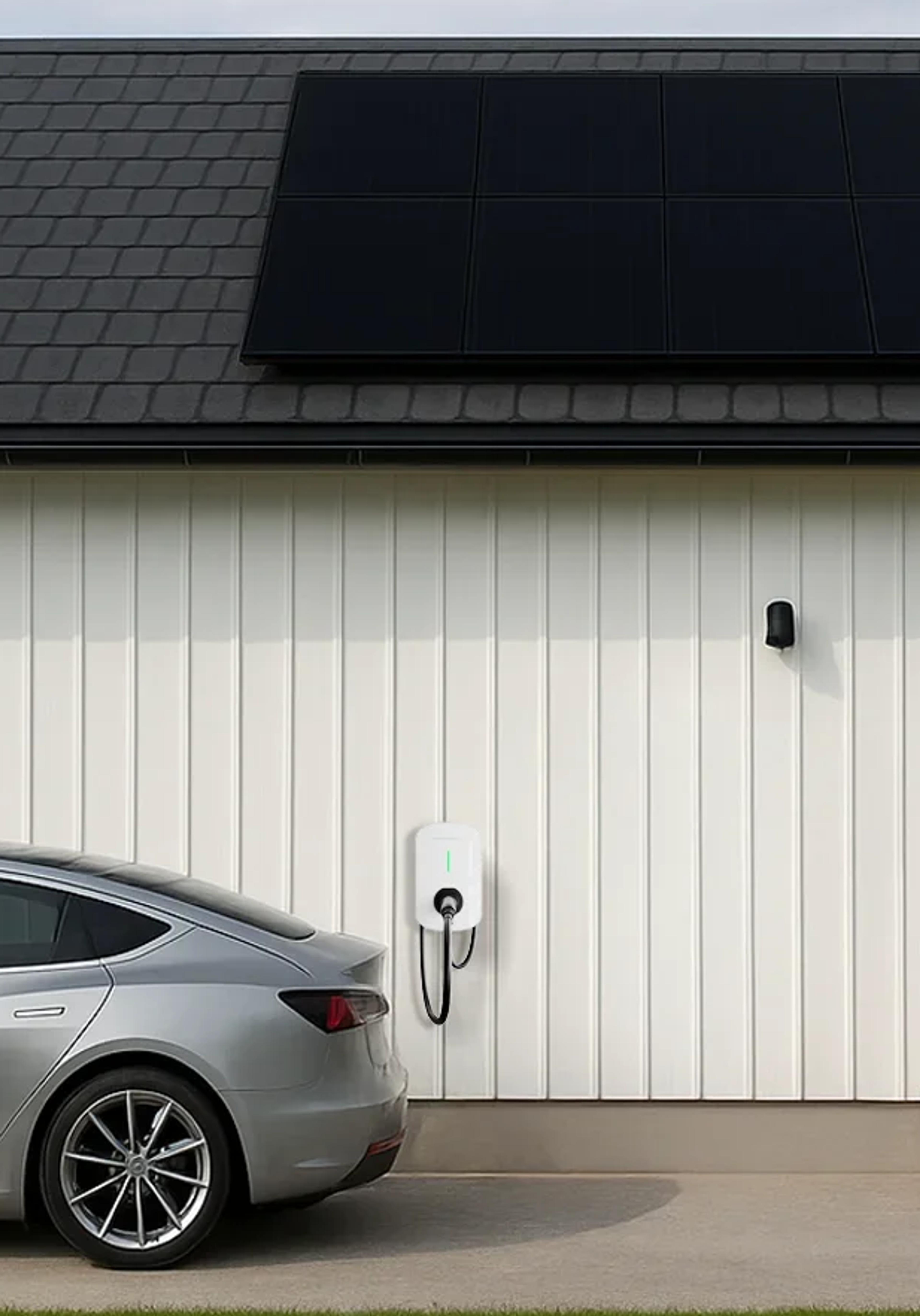 En bil lader utenfor et hvitt hus med solceller på taket