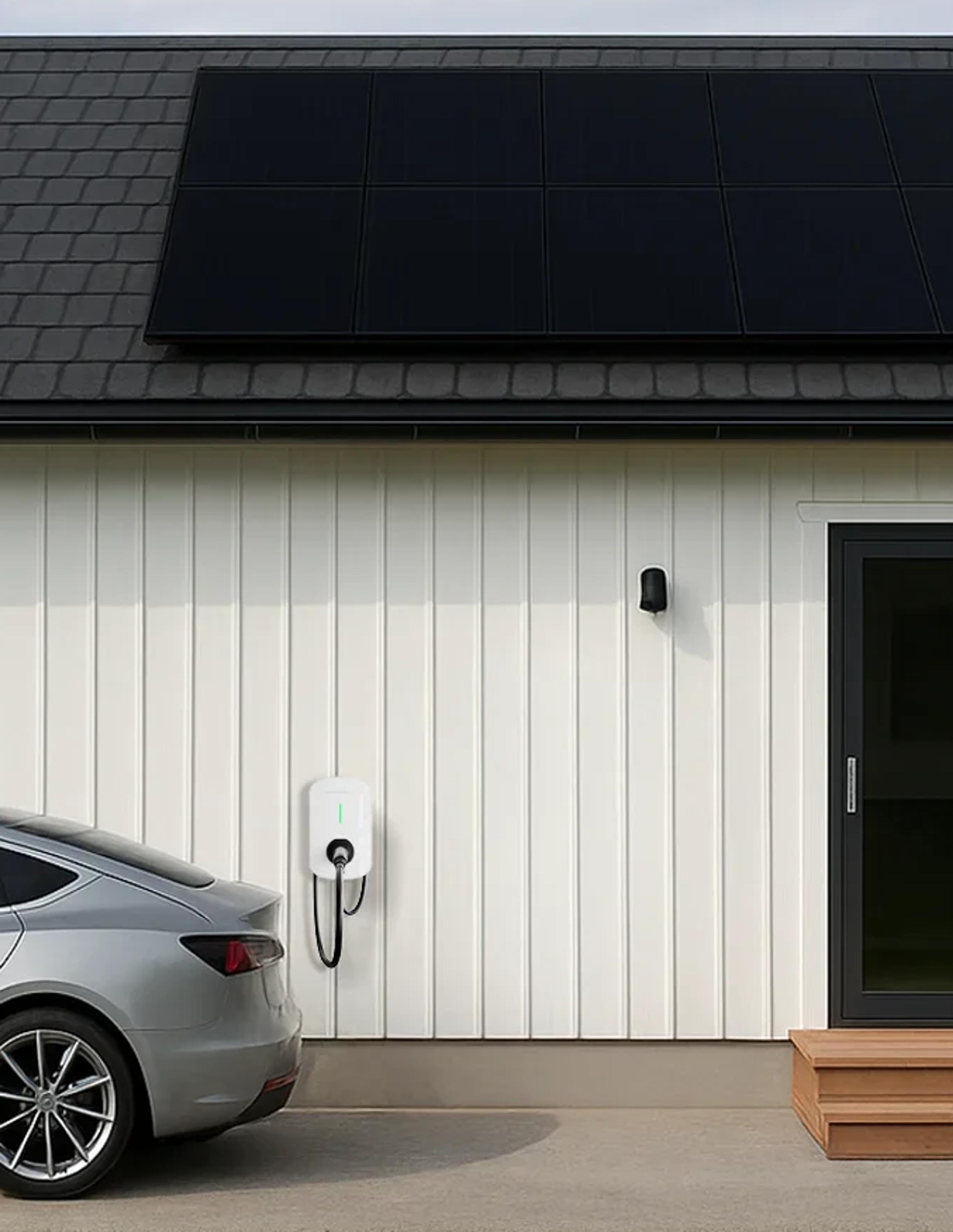 En bil lader fra en ladeboks montert på ytterveggen på et hus med solceller på taket
