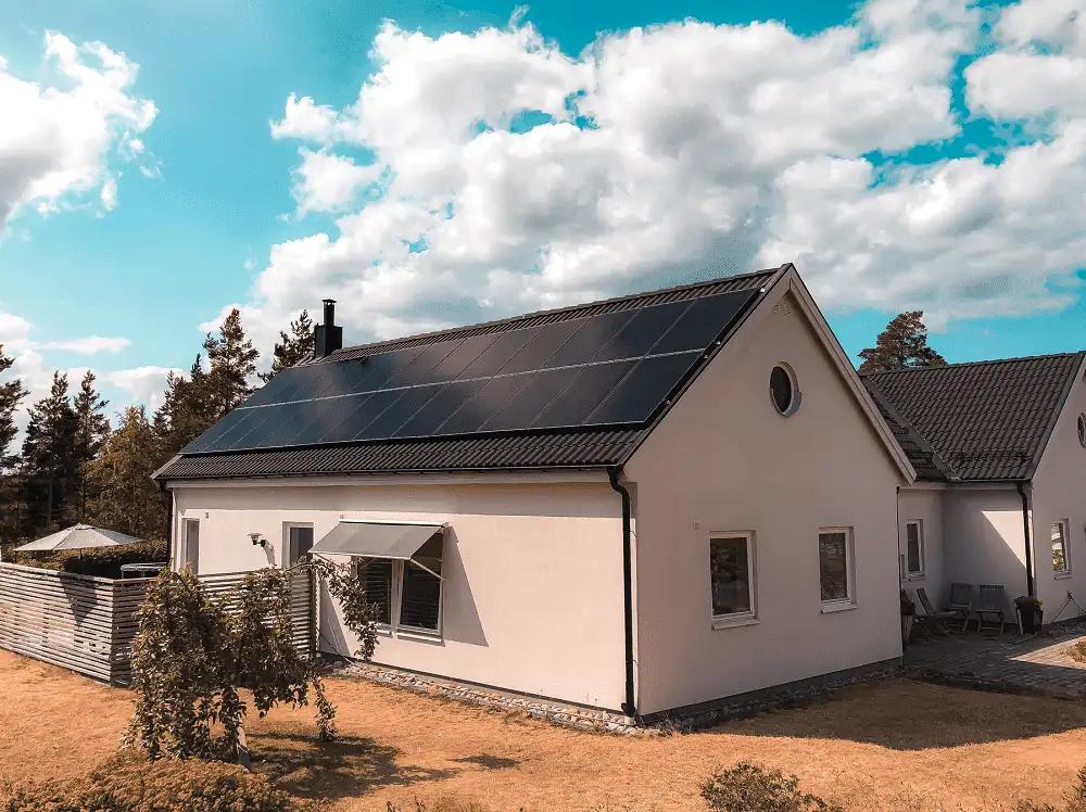 hus med vit putsad fasad som har svarta solceller på taket