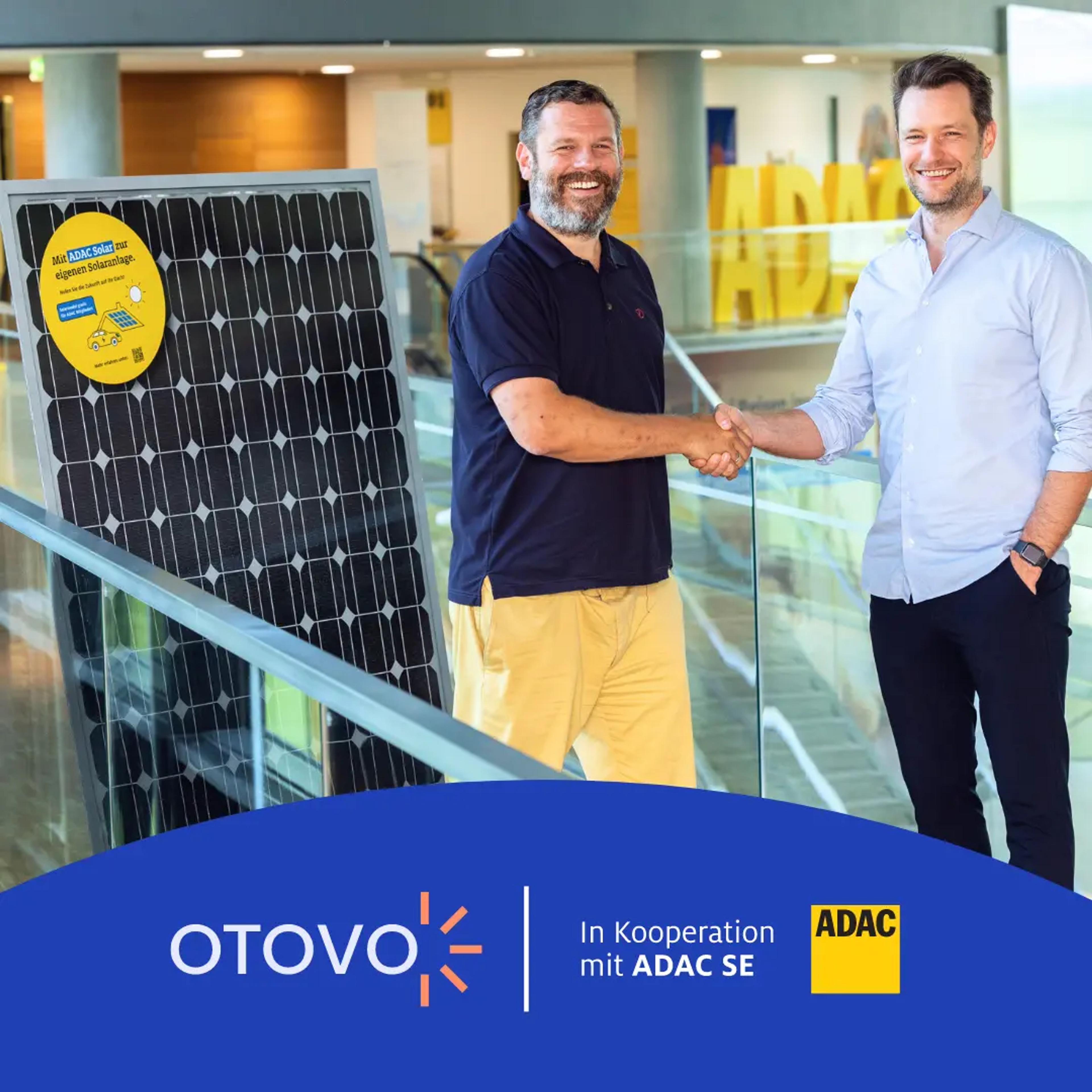 Vertreter von ADAC und Otovo geben sich vor einem Solarmodul die Hand.