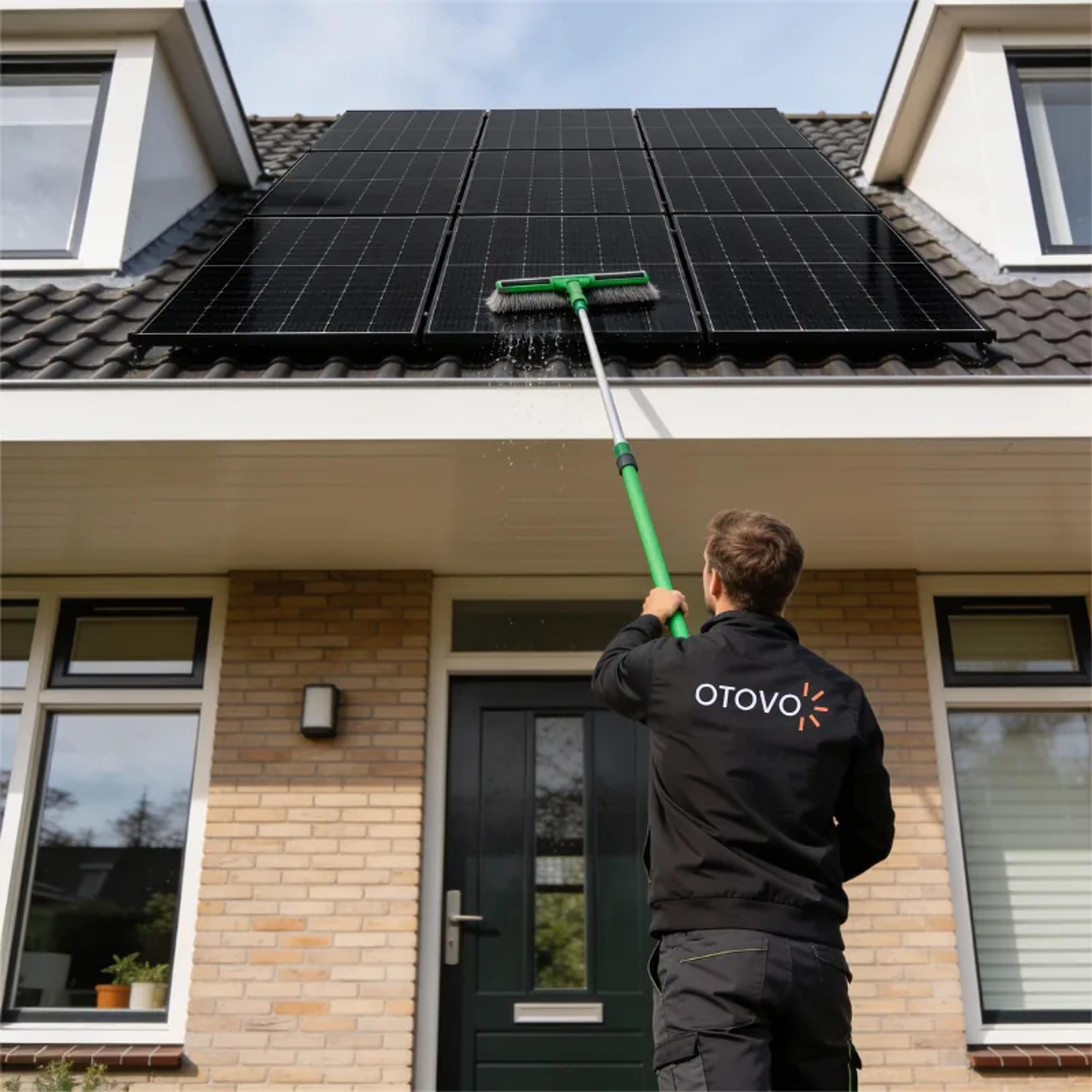 Otovo-monteur reinigt zonnepanelen op een dak met een wasborstel op een telescoopsteel