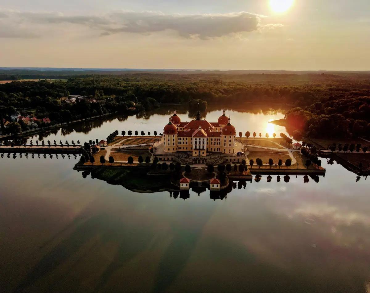 Ein Schloss an einem See in Sachsen, mit dem Sonnenuntergang im Hintergrund.