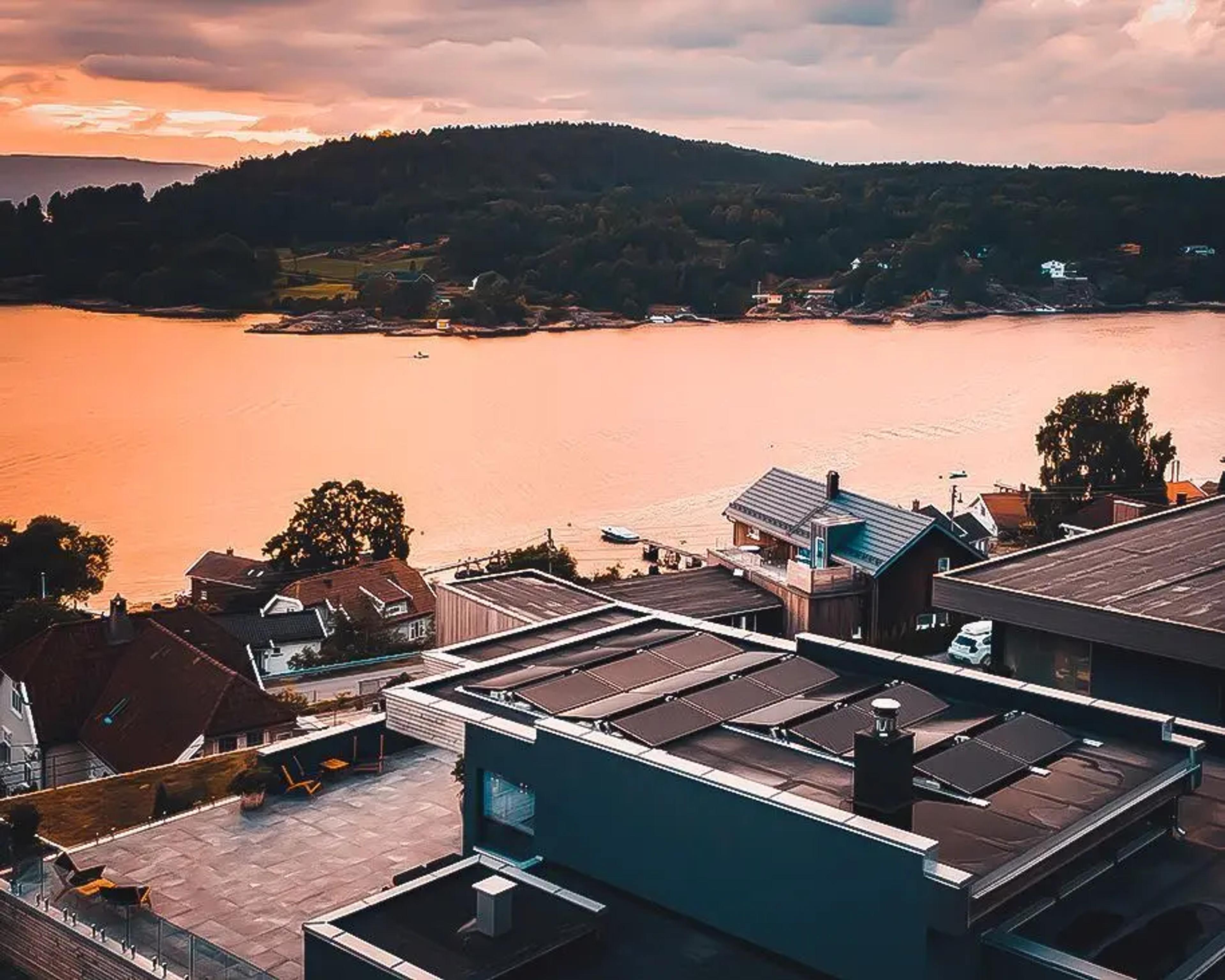 et hus ved vannkanten som har solcellepaneler montert på et flatt tak