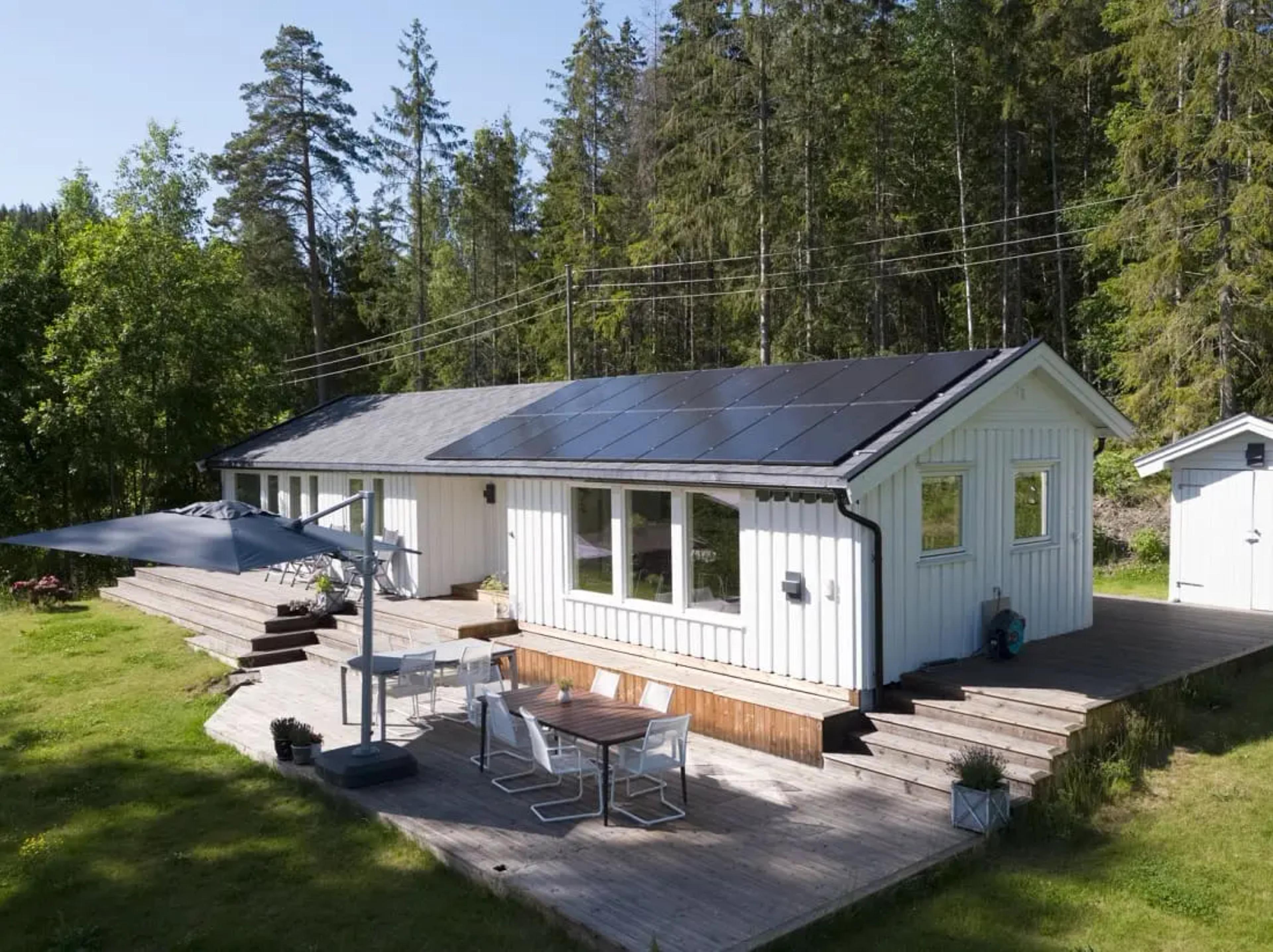 vitt enplanhus i skogsområde med terrass och solceller på taket