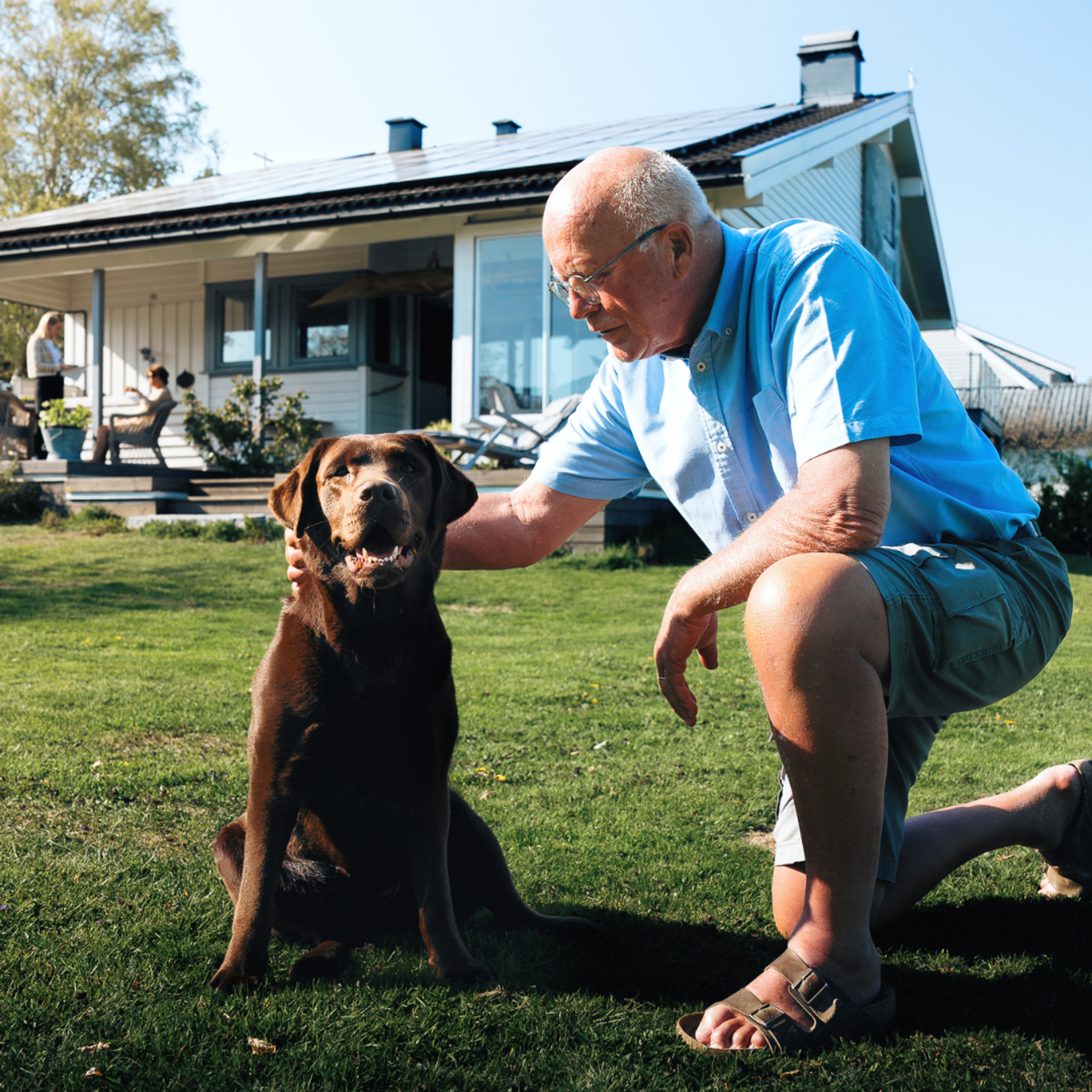 Haus mit Photovoltaikanlage auf dem Dach und Besitzer mit Hund im Vordergrund