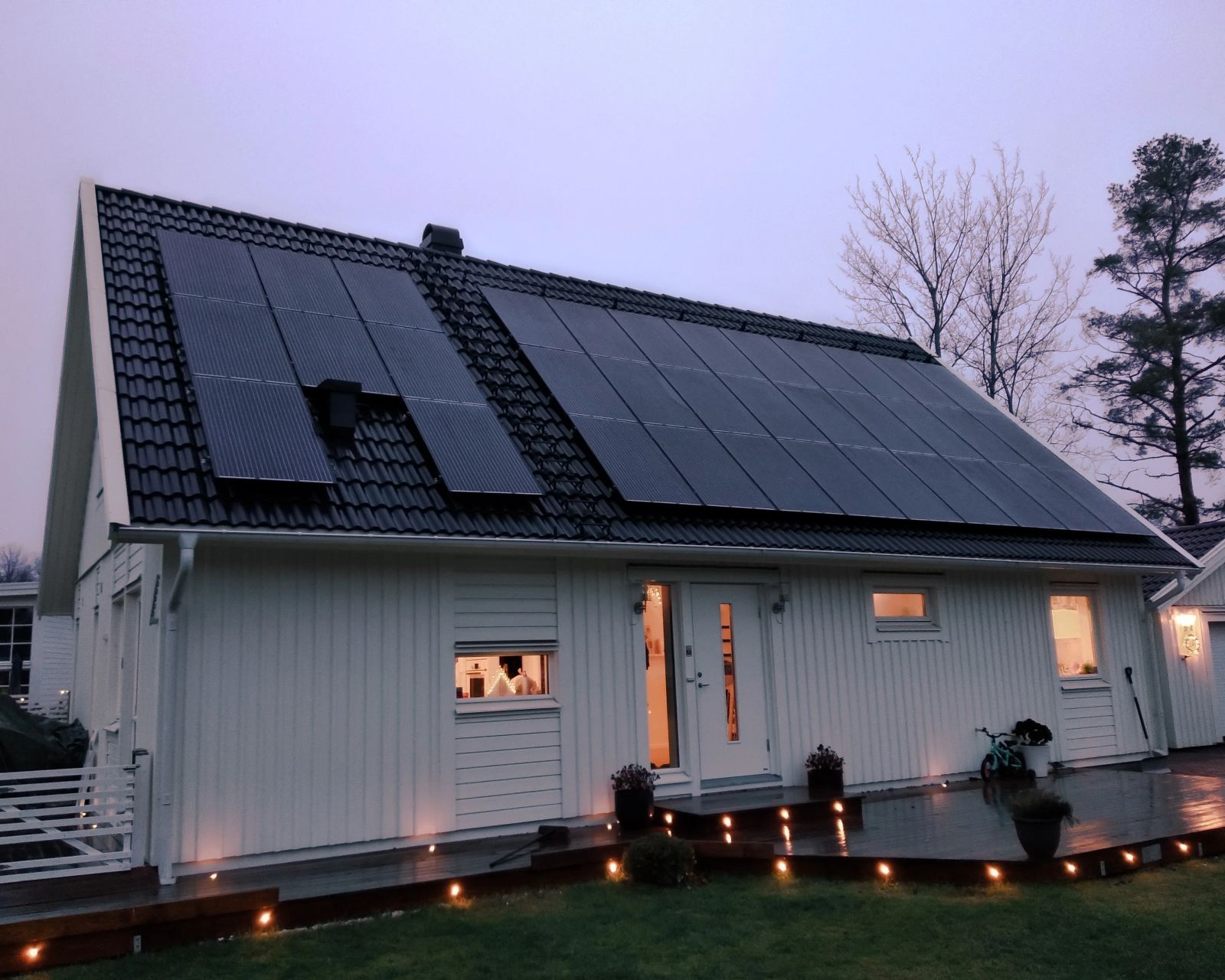 Et hus med solcellepaneler på taket i skumring, med hyggelig lys fra vinduene