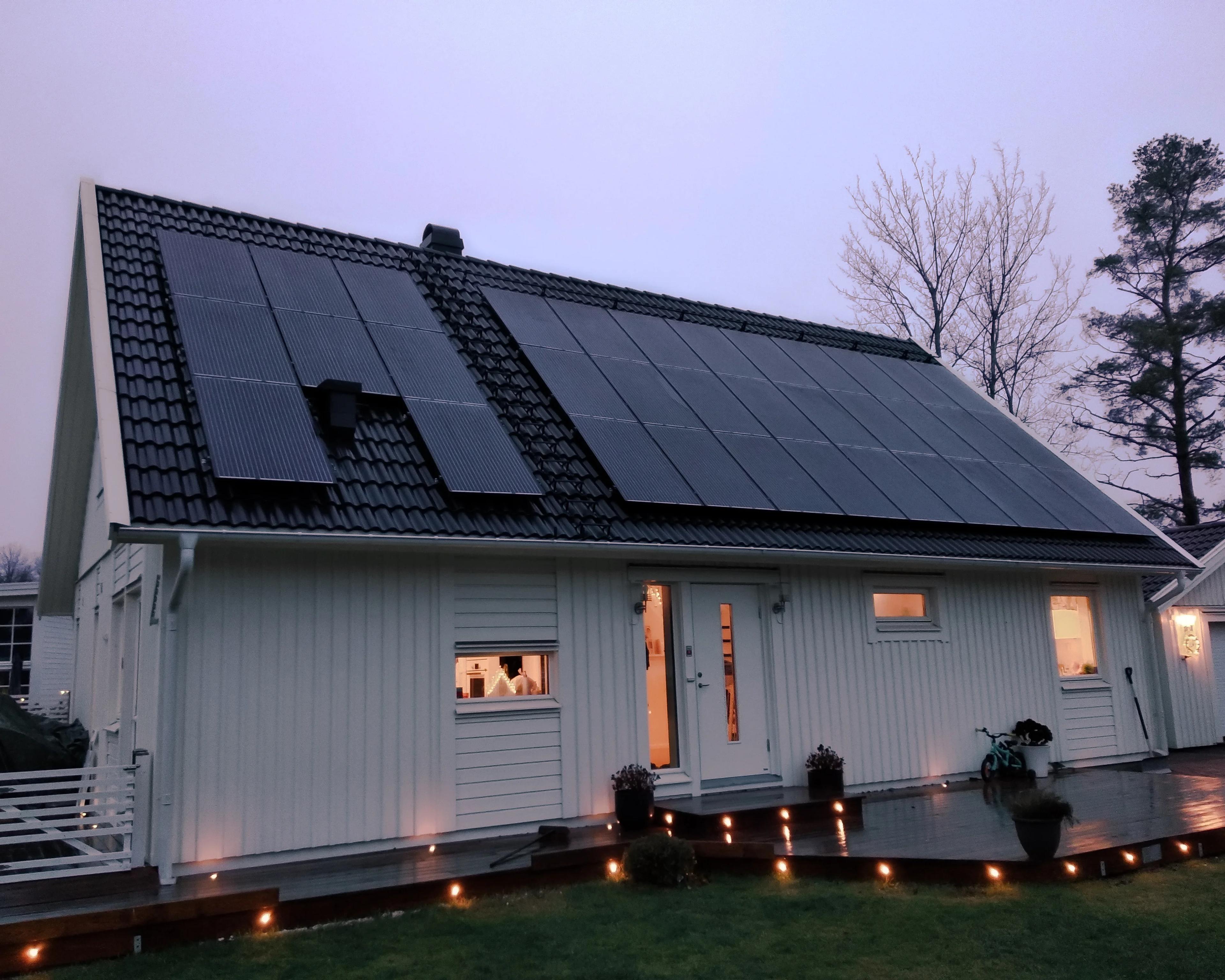 Et hus med solcellepaneler på taket i skumring, med hyggelig lys fra vinduene
