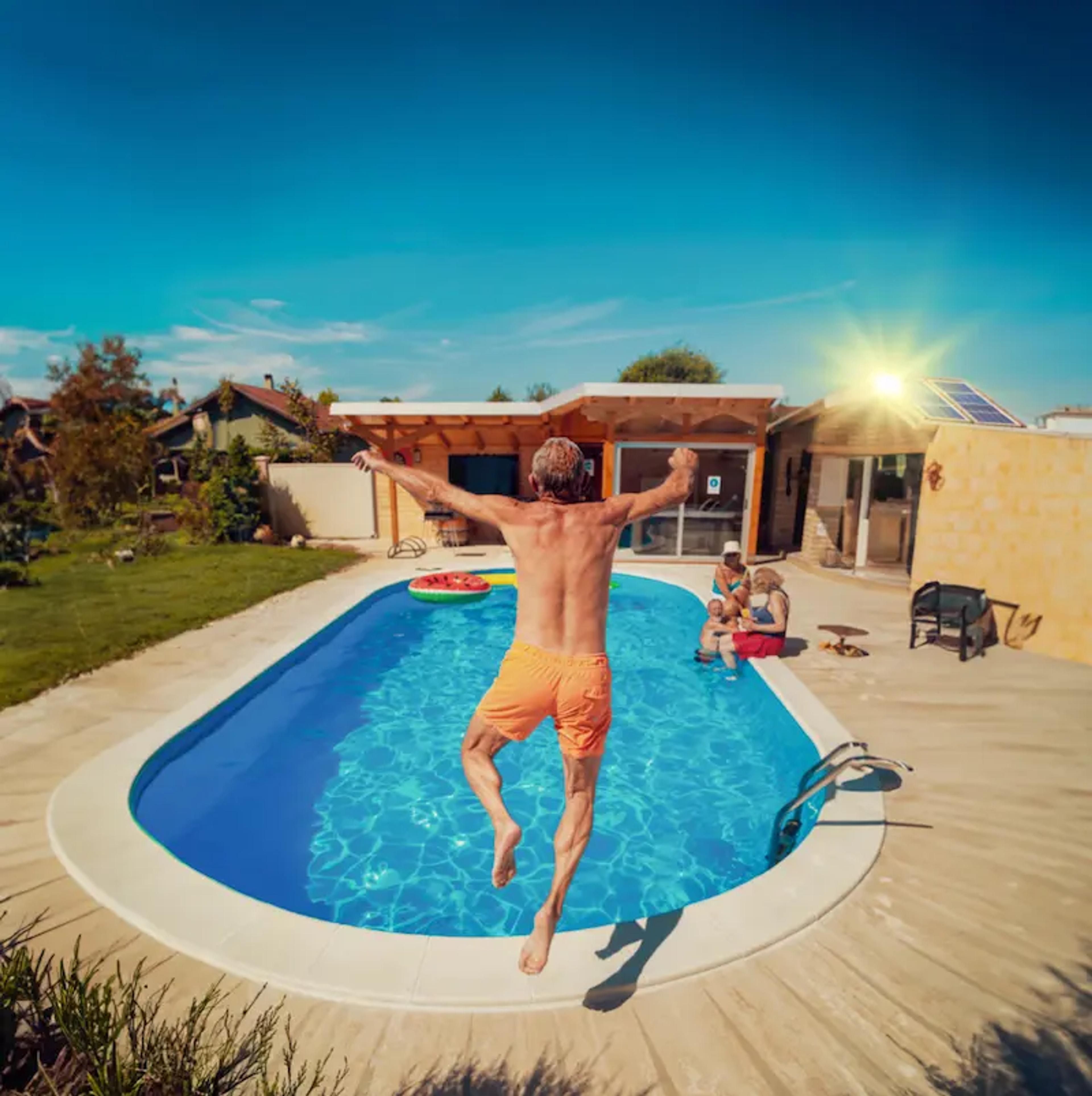 homme sautant dans une piscine avec sa maison équipée de panneaux solaires au loin