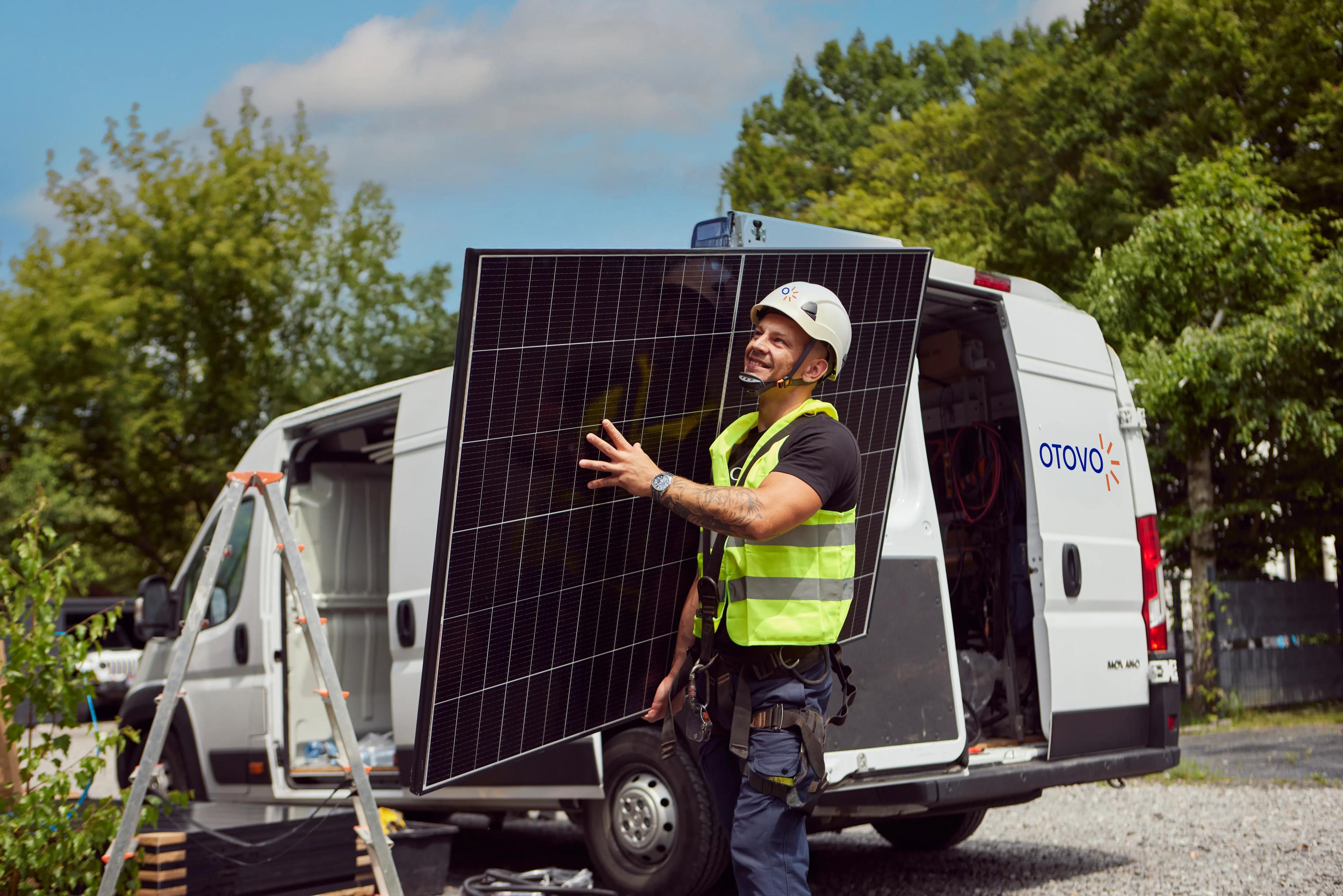 Instalador transportando un panel solar desde una furgoneta