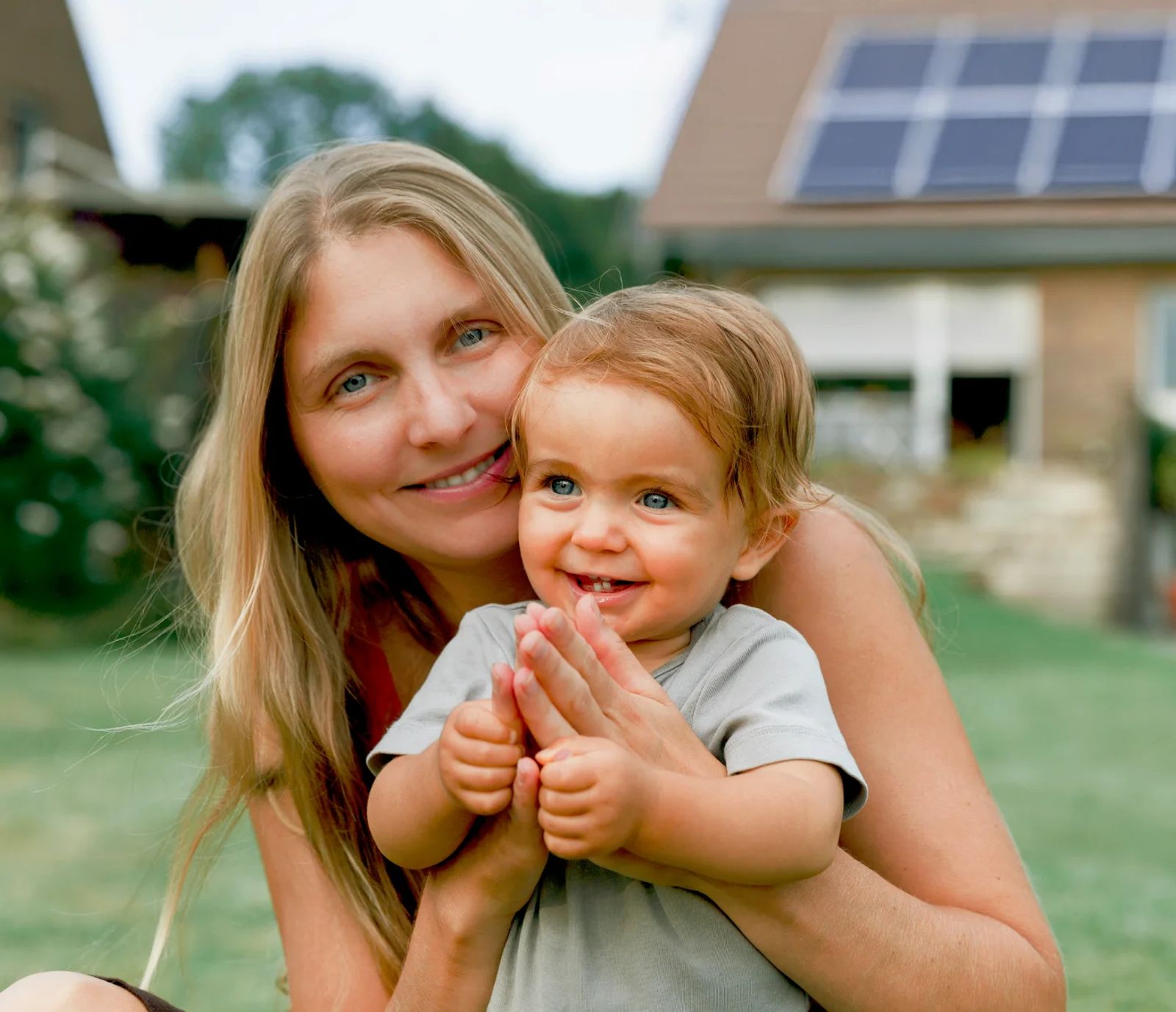 Mutter und Kind mit einem Haus mit Photovoltaik im Hintergrund