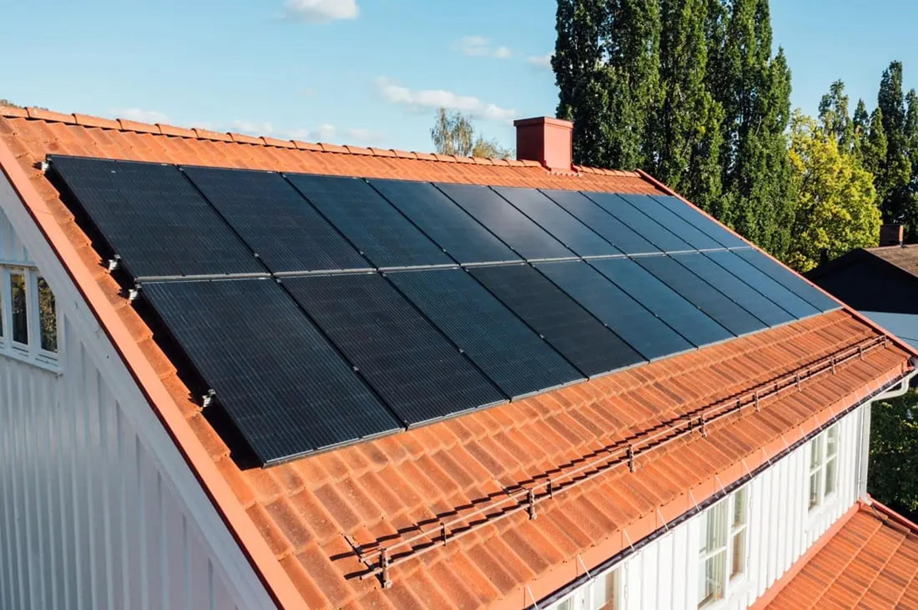 nærbilde av solcellepaneler på et hvitt hus med takstein