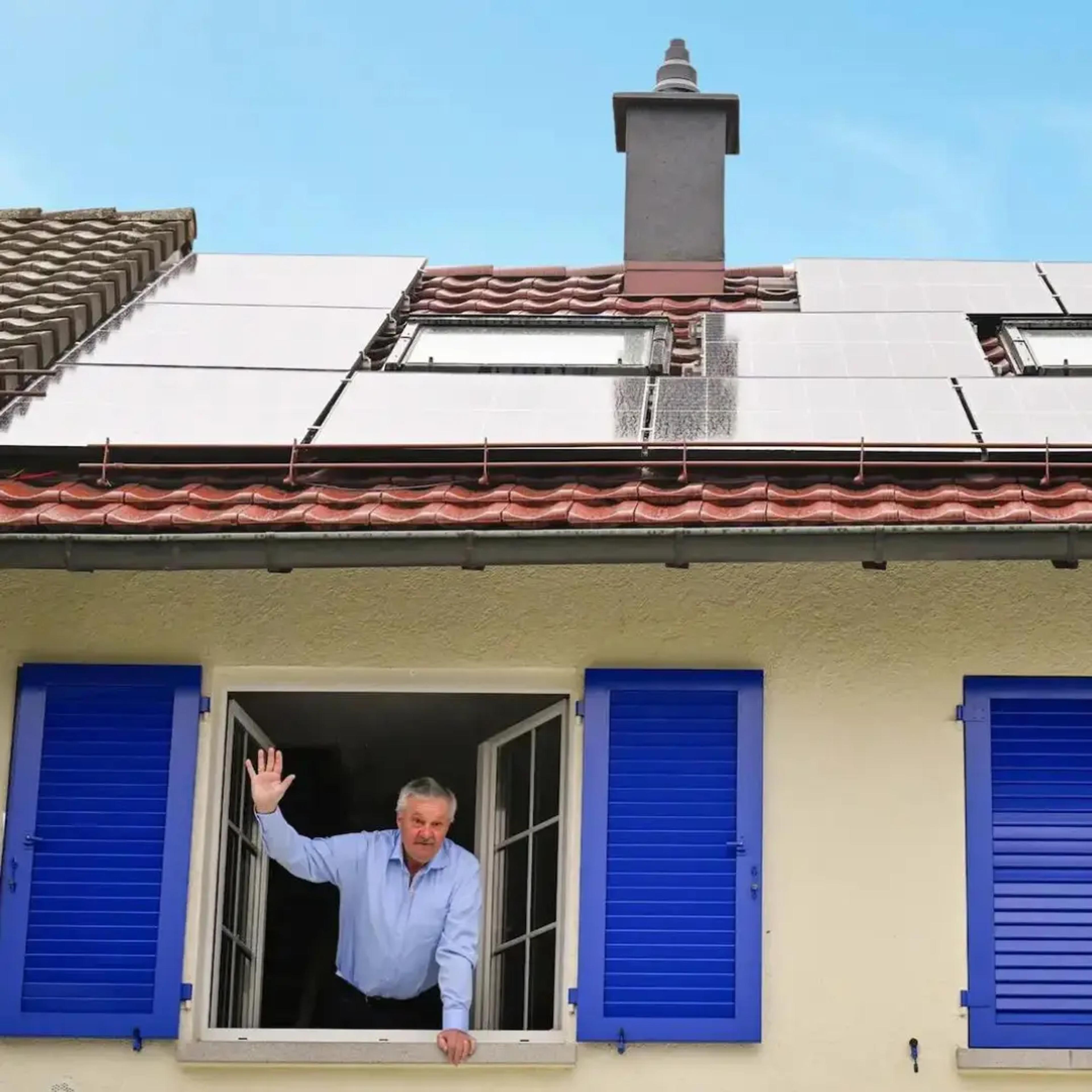 Ein Otovo Kunde steht im Fenster eines Hauses, auf dem eine Solaranlage installiert ist.