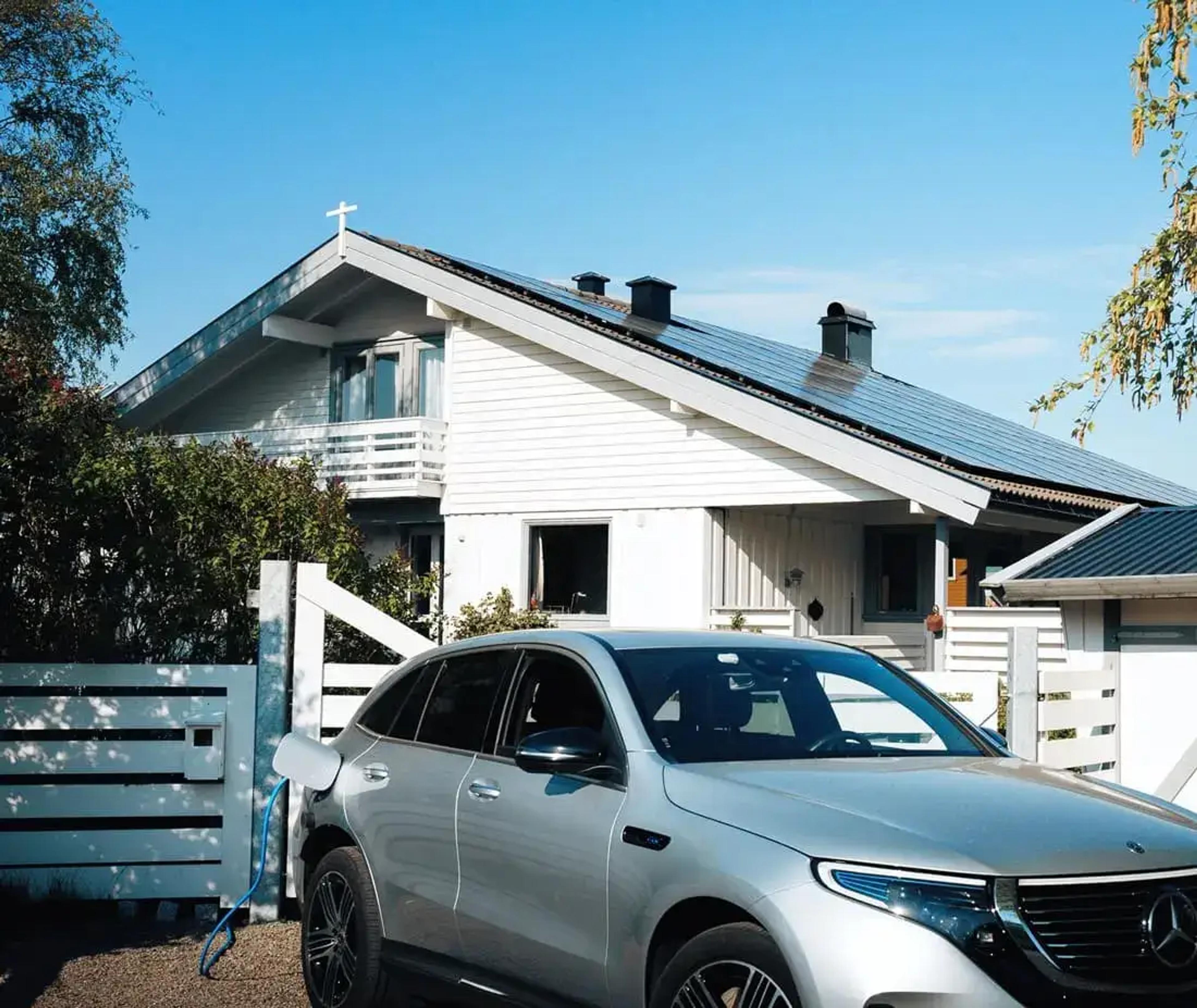 elbil i garasjeoppkjørselen foran et hvitt hus med solceller på taket