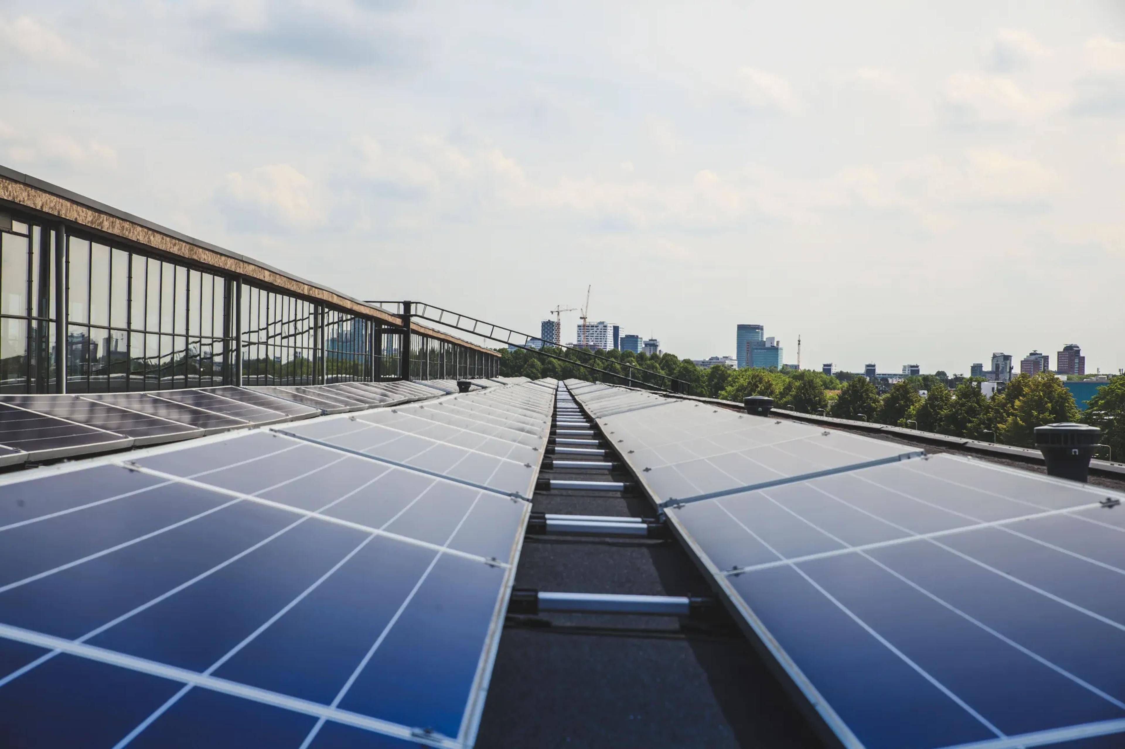 Solar panel array on a roof in a city. Tower buildings can be seen in the distance.