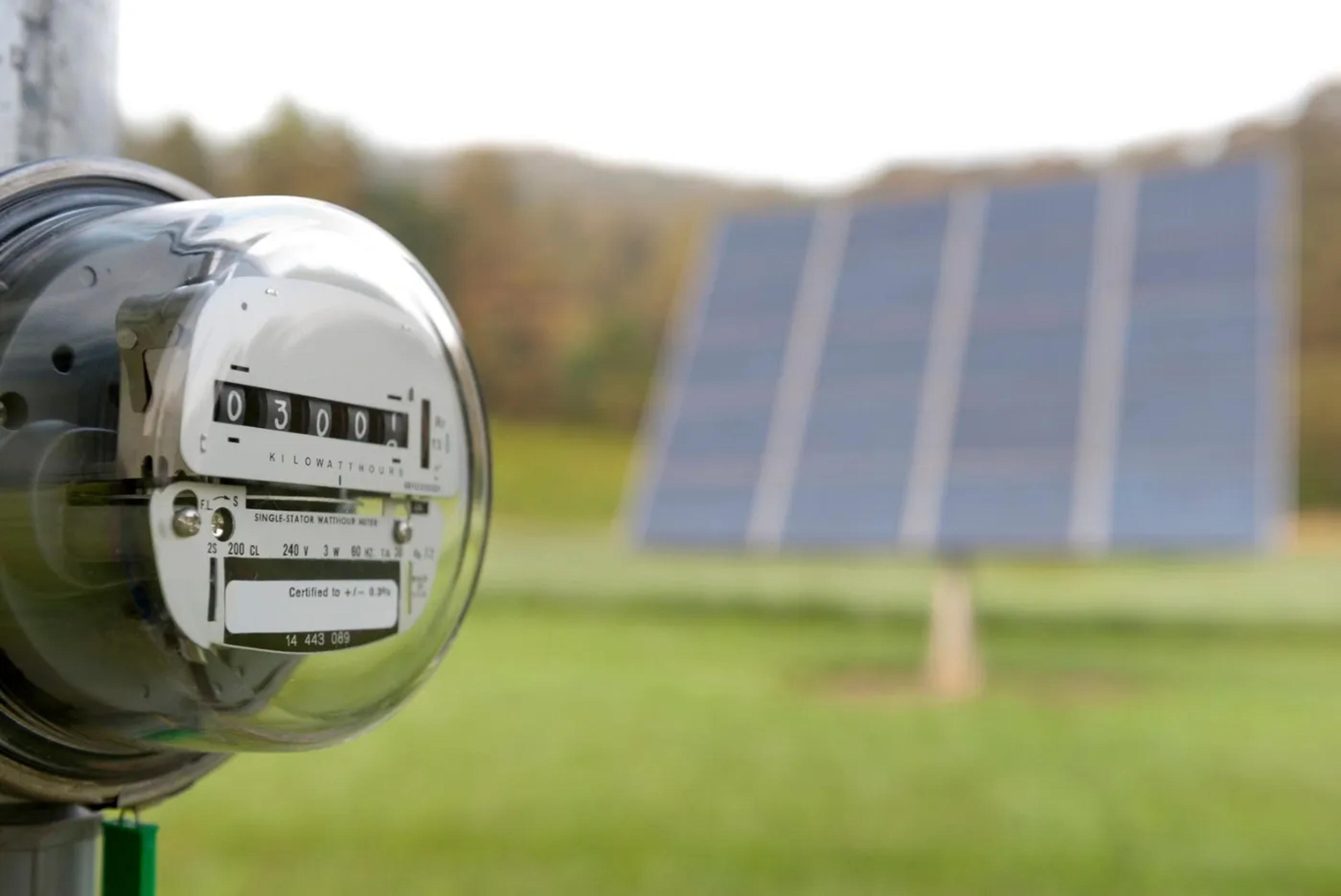 Een analoge terugdraaiende meter met zonnepanelen op de achtergrond