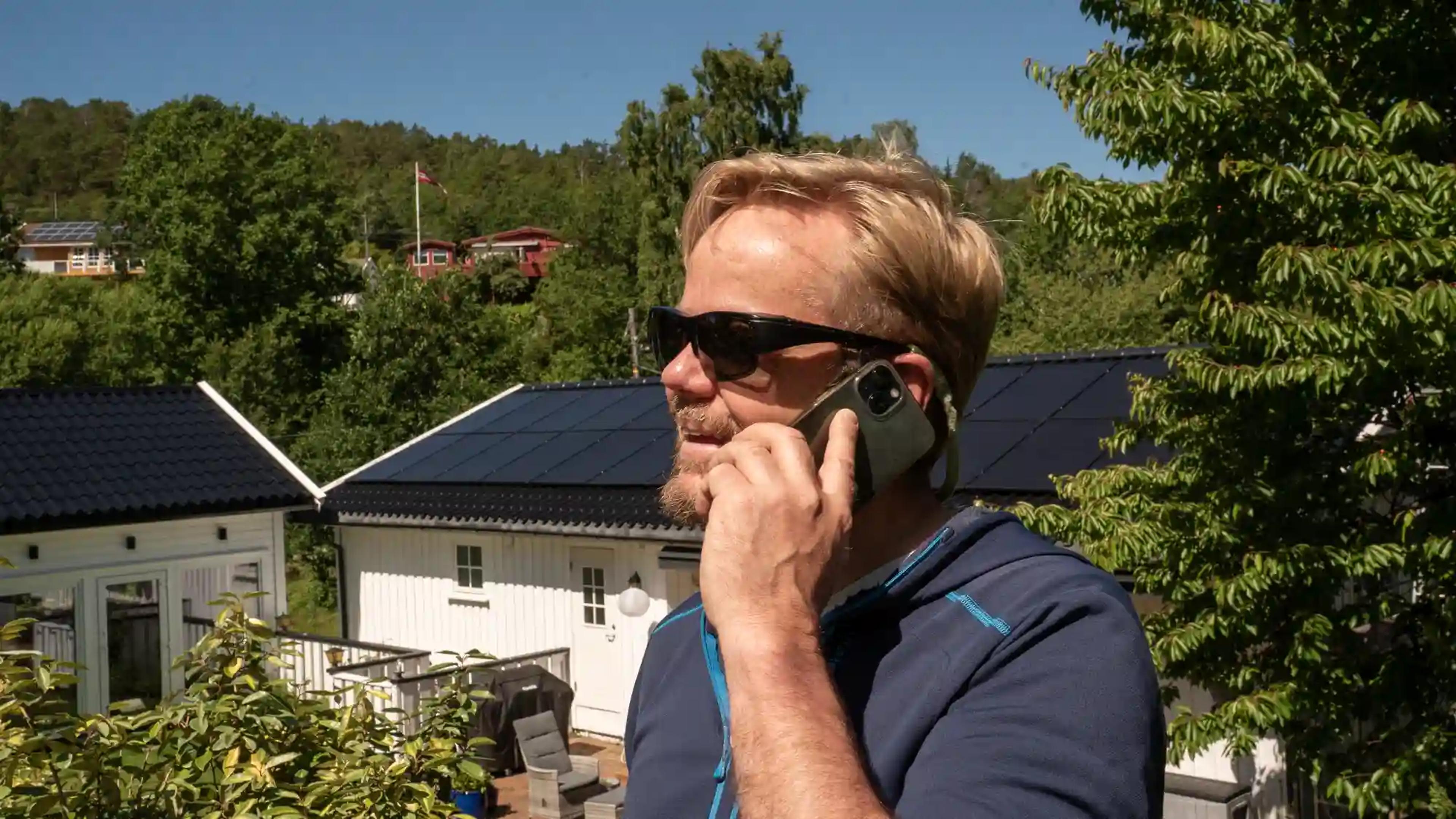 mann snakker i telefon foran huset sitt med solcellepaneler på taket