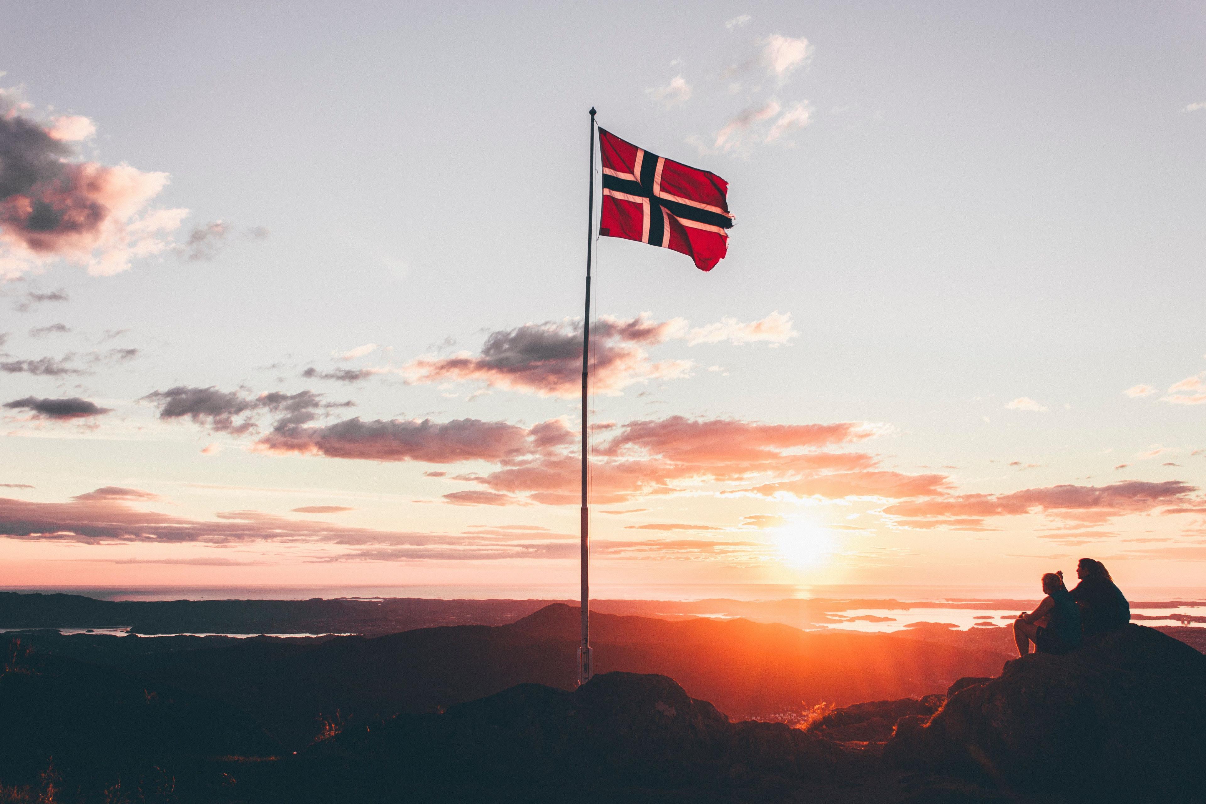 mennesker på en klippe og norsk flagg i vinden