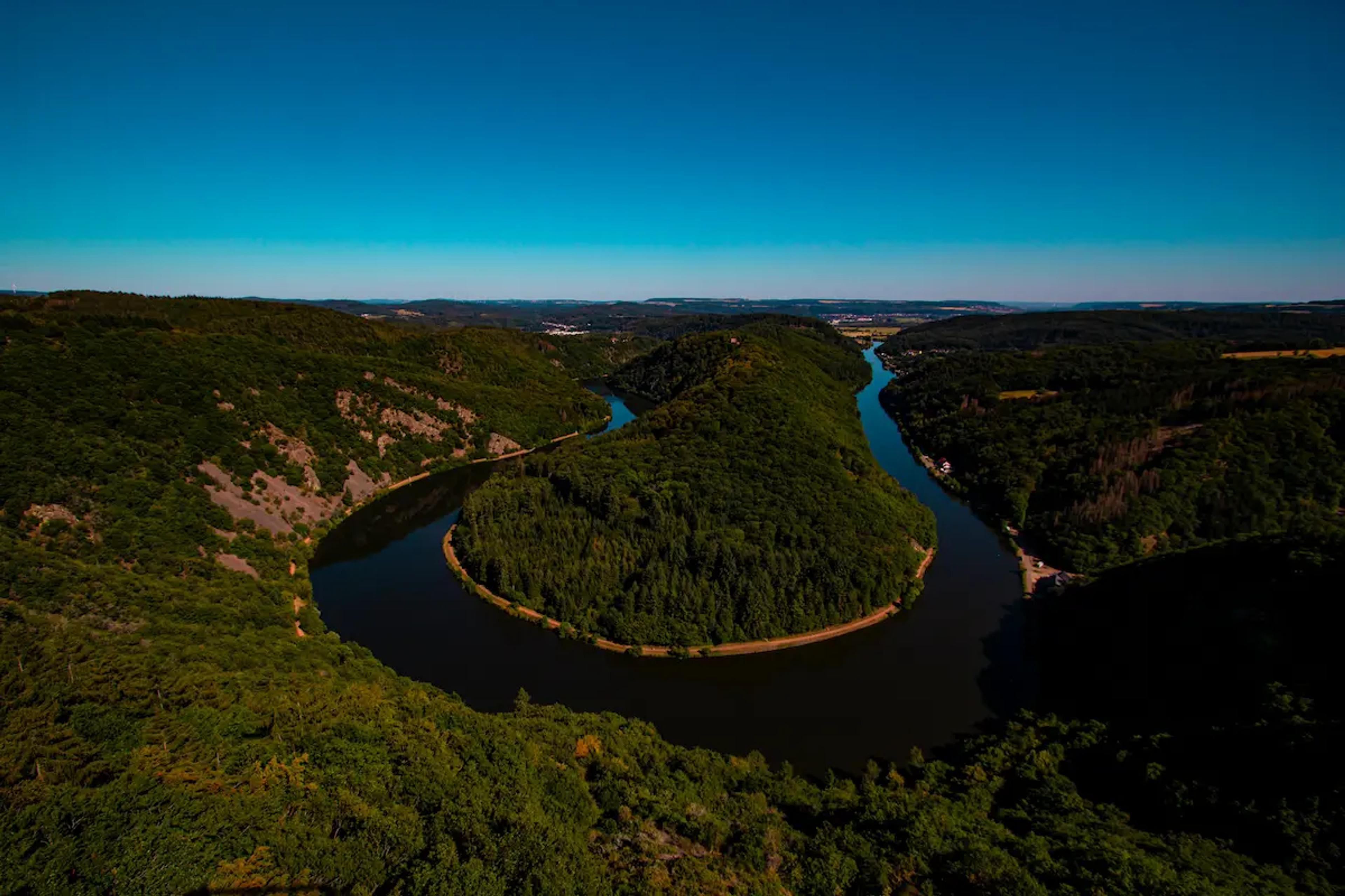 Ein grüner Hügel in der Sonne umgeben von einem Fluss im Saarland.