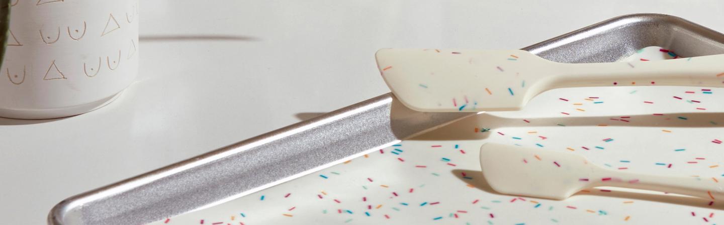 An up close shot of the sprinkles baking mat on a baking sheet with two kitchen tools with the sprinkles pattern.