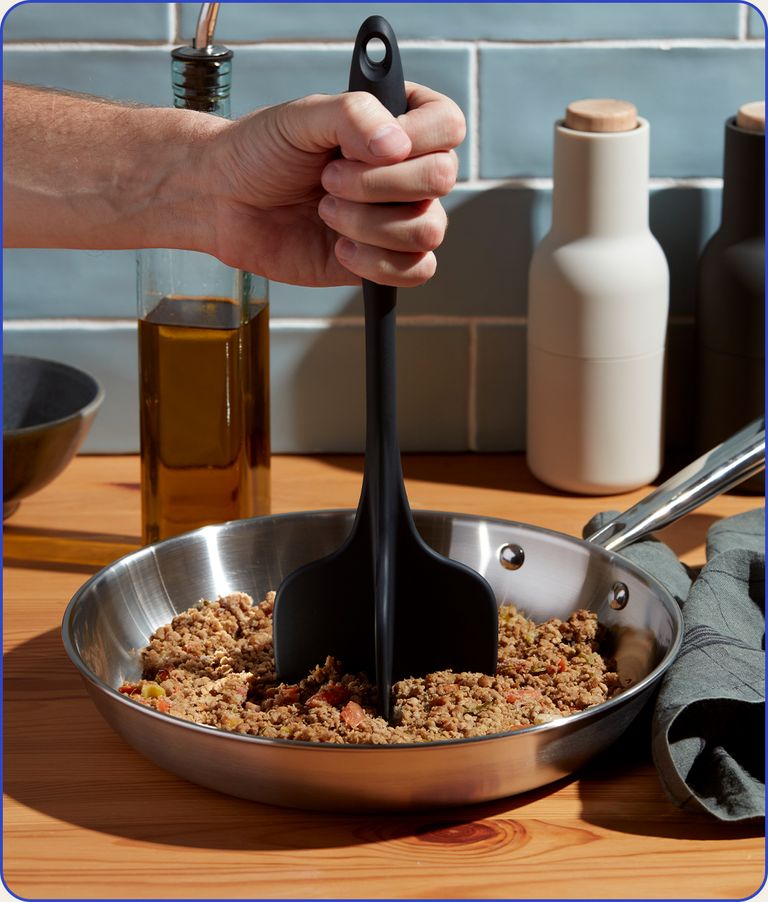 A hand holding the GIR quad chopper in a pan of ground meat.
