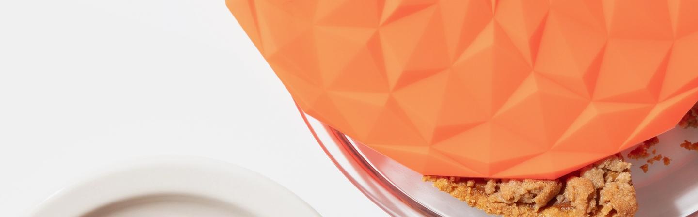 A corner shot of a pie dish with an orange suction lid over.
