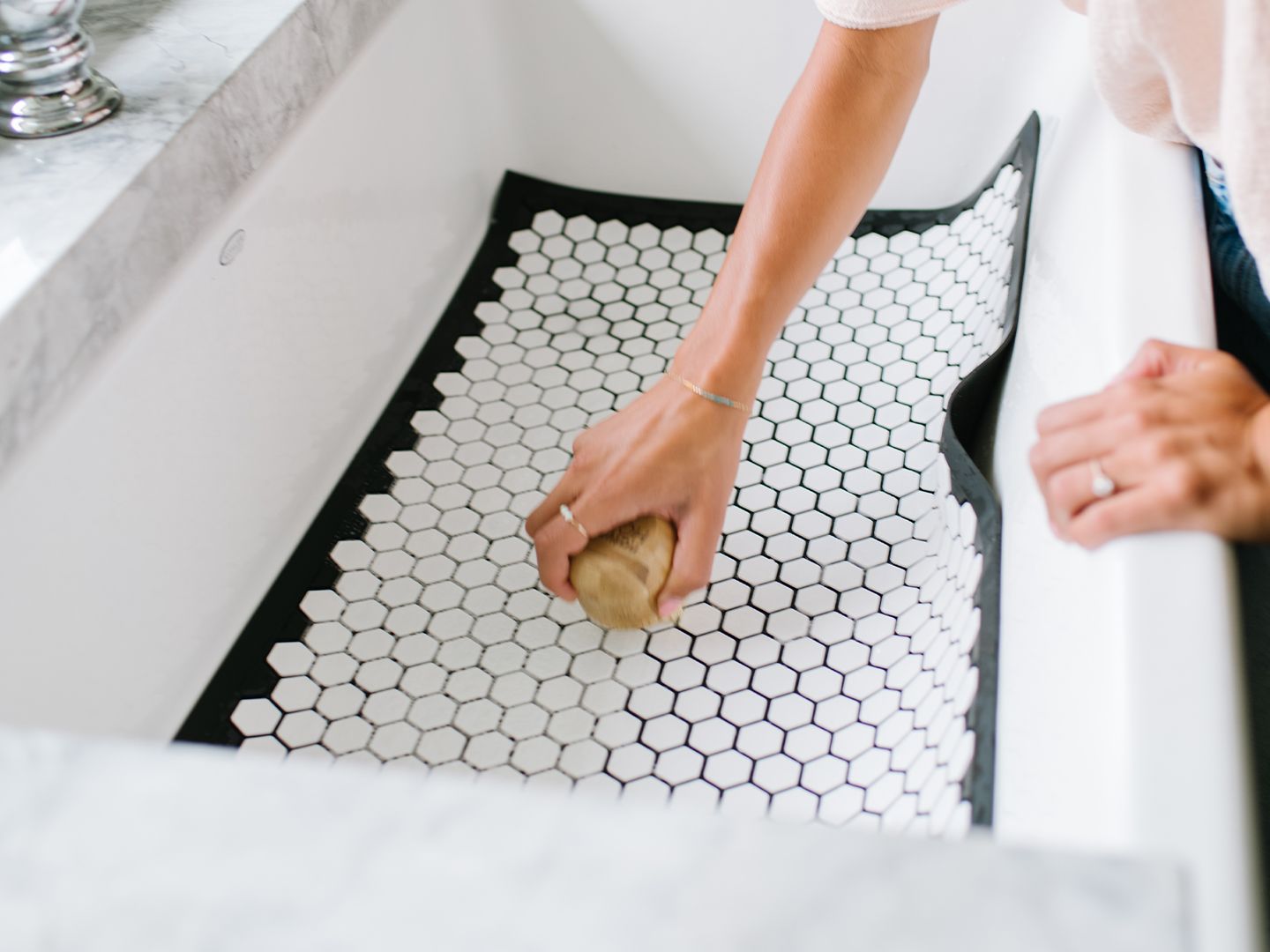 A person cleaning a tile mat in a bath tub