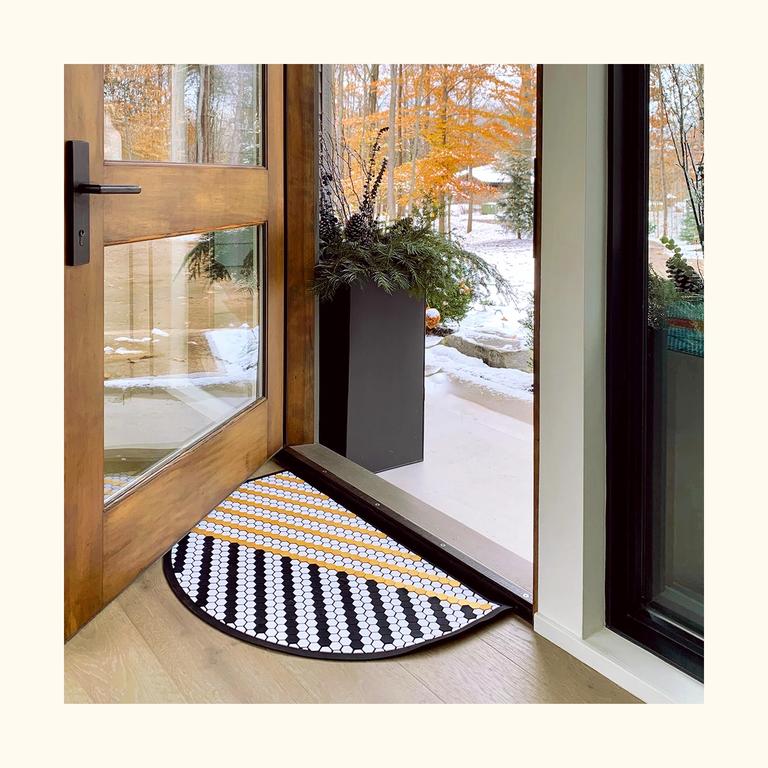 The Half Moon Tile Mat with a yellow and black striped design in a front door entryway.