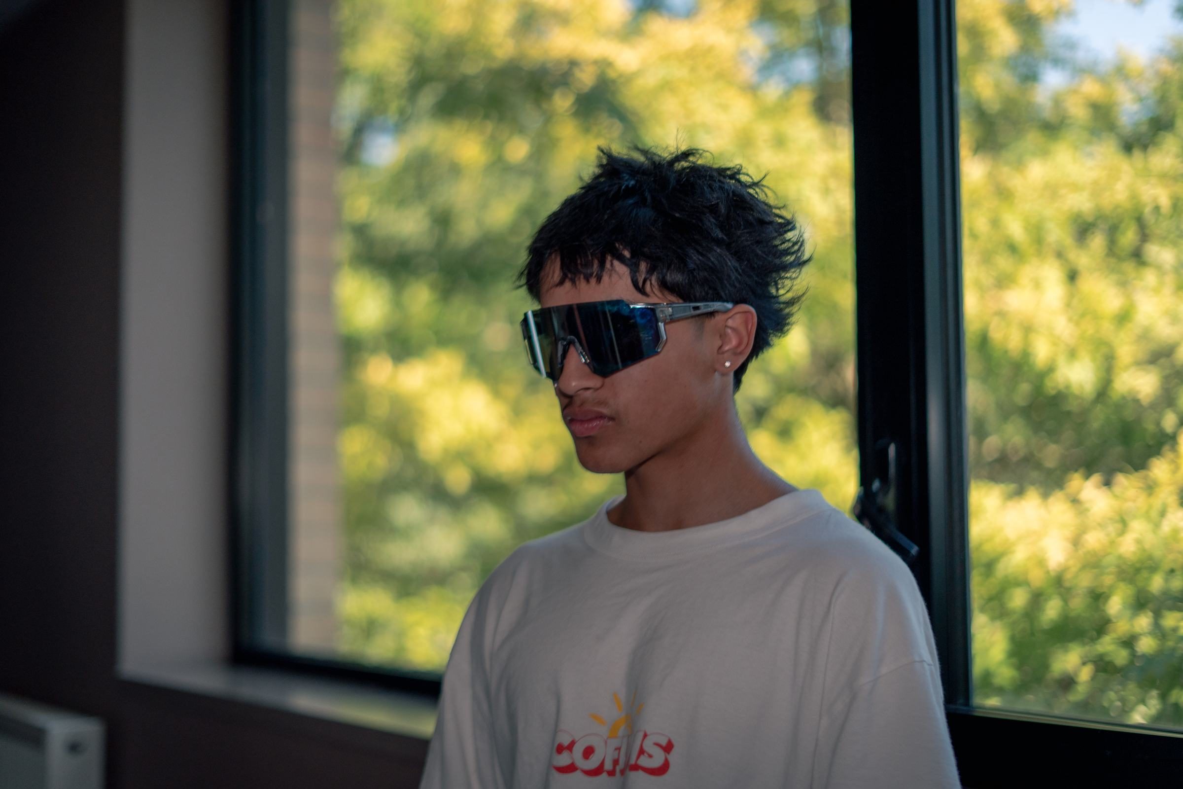 Portrait d'un participant en lunettes masque, devant une baie ouverte sur les arbres