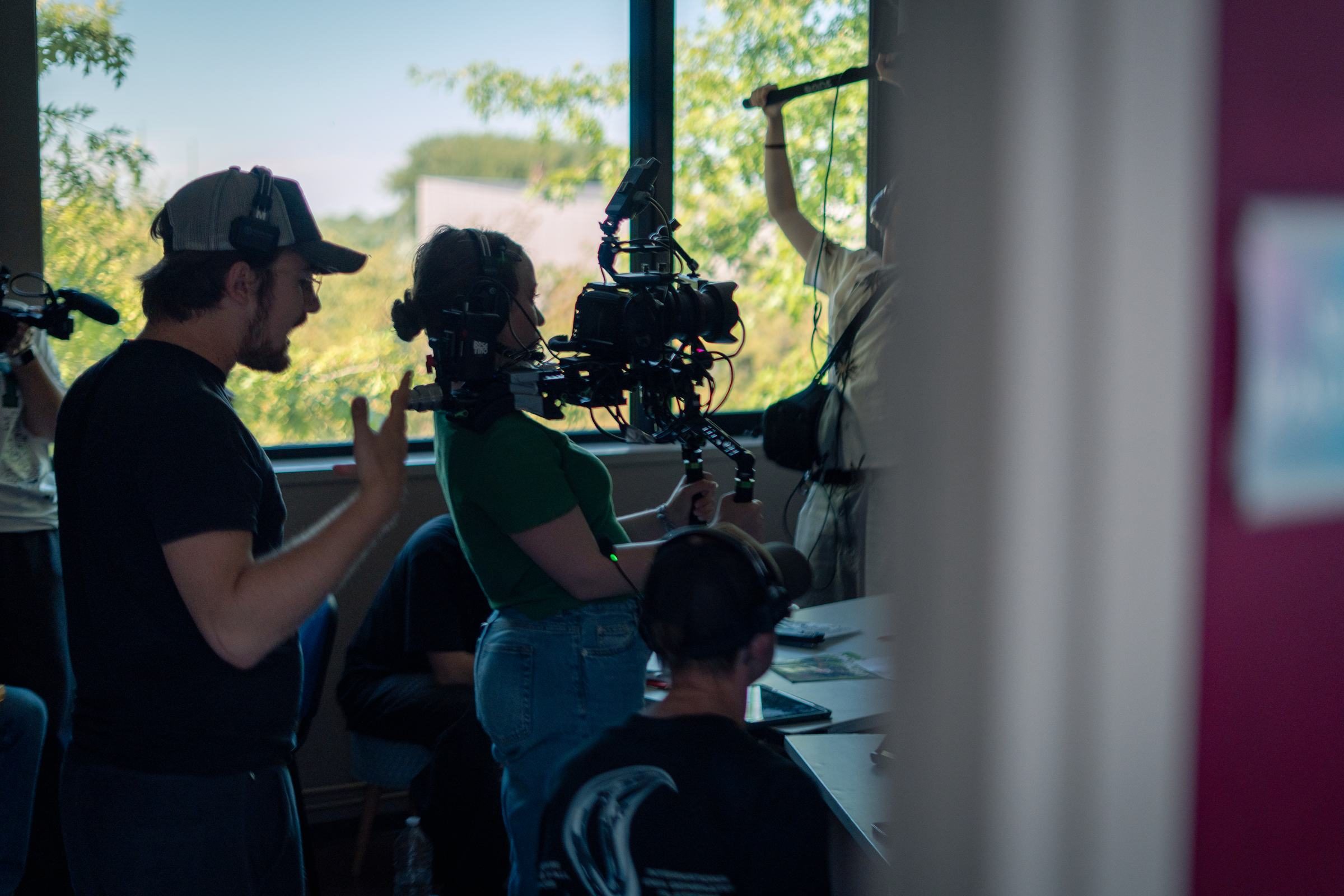 Une equipe de tournage au travail : cadreuse a l'epaule, perchman bras leve, realisateur qui indique le cadre