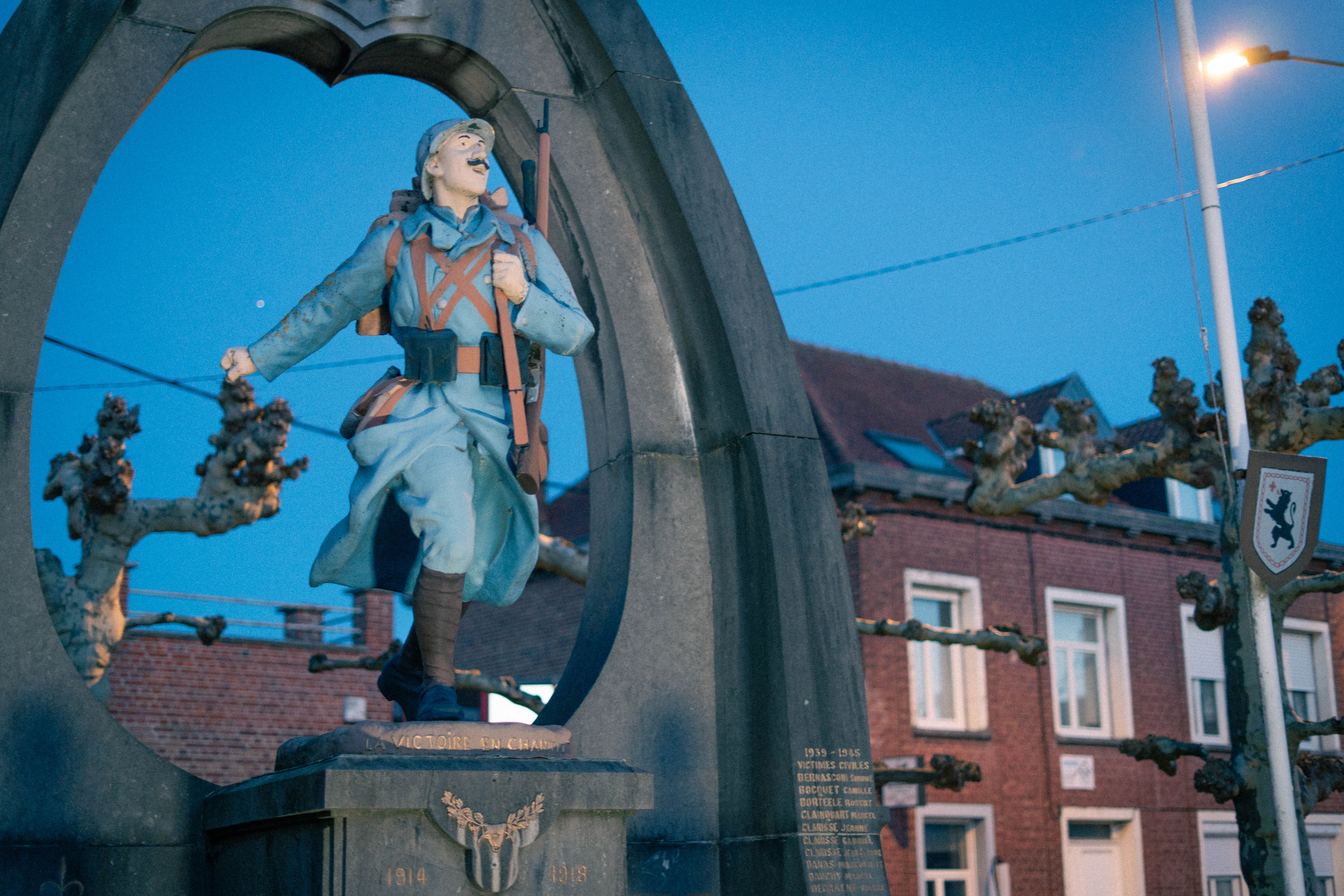 La statue d'un soldat, cadrée par l'arche du monument aux morts, à l'heure bleue