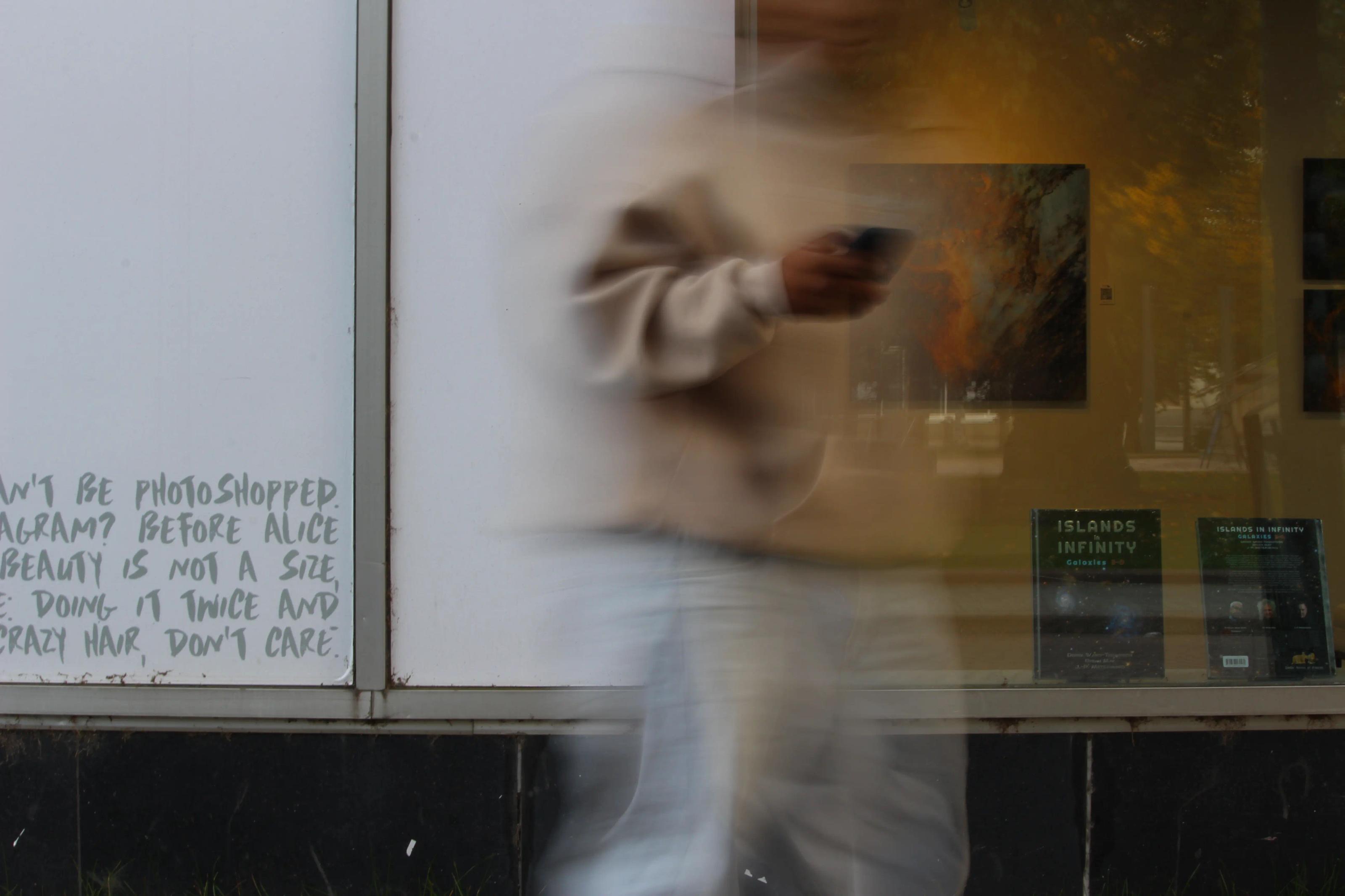 The photo shows a person scrolling through their phone; the image is slightly blurred as part of the artistic design.