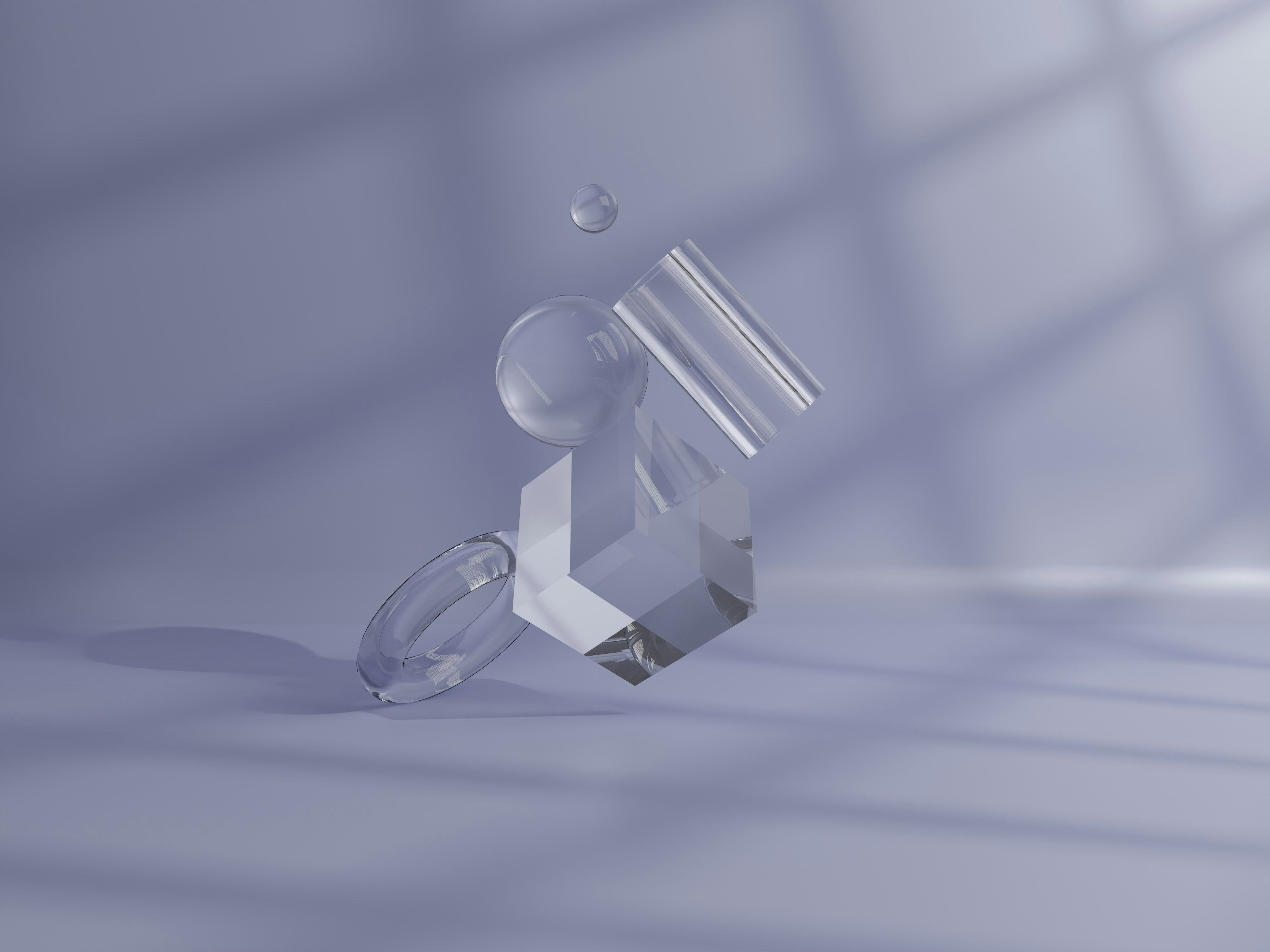 Transparent glass geometric shapes on a pale violet surface in the shadow of a window.
