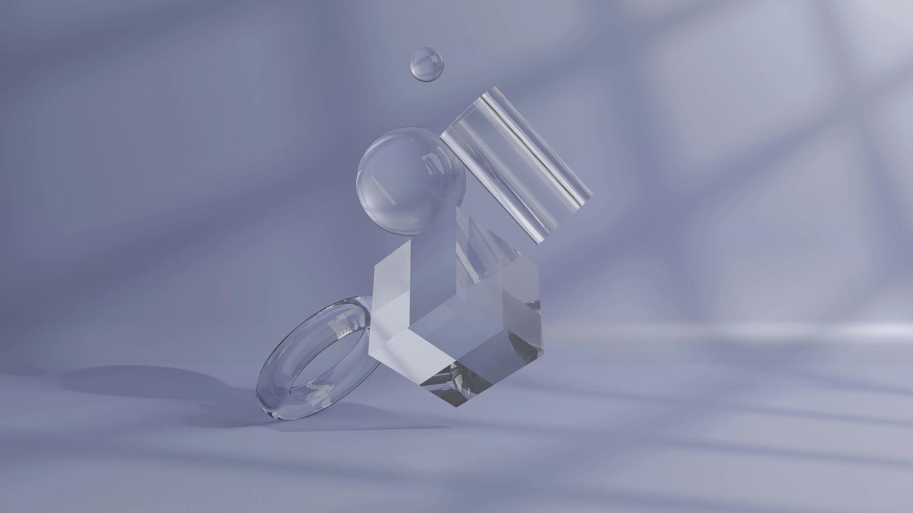 Transparent glass geometric shapes on a pale violet surface in the shadow of a window.