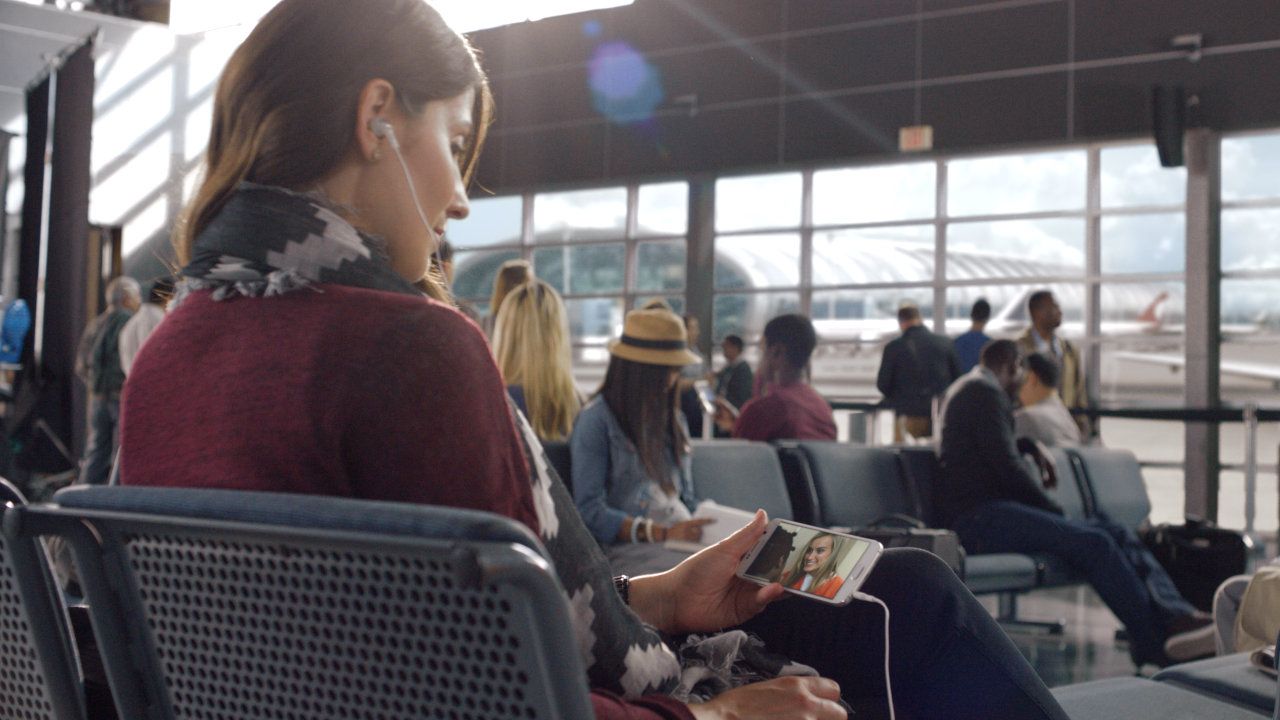 A woman watches a Netflix show on a mobile device at the airport