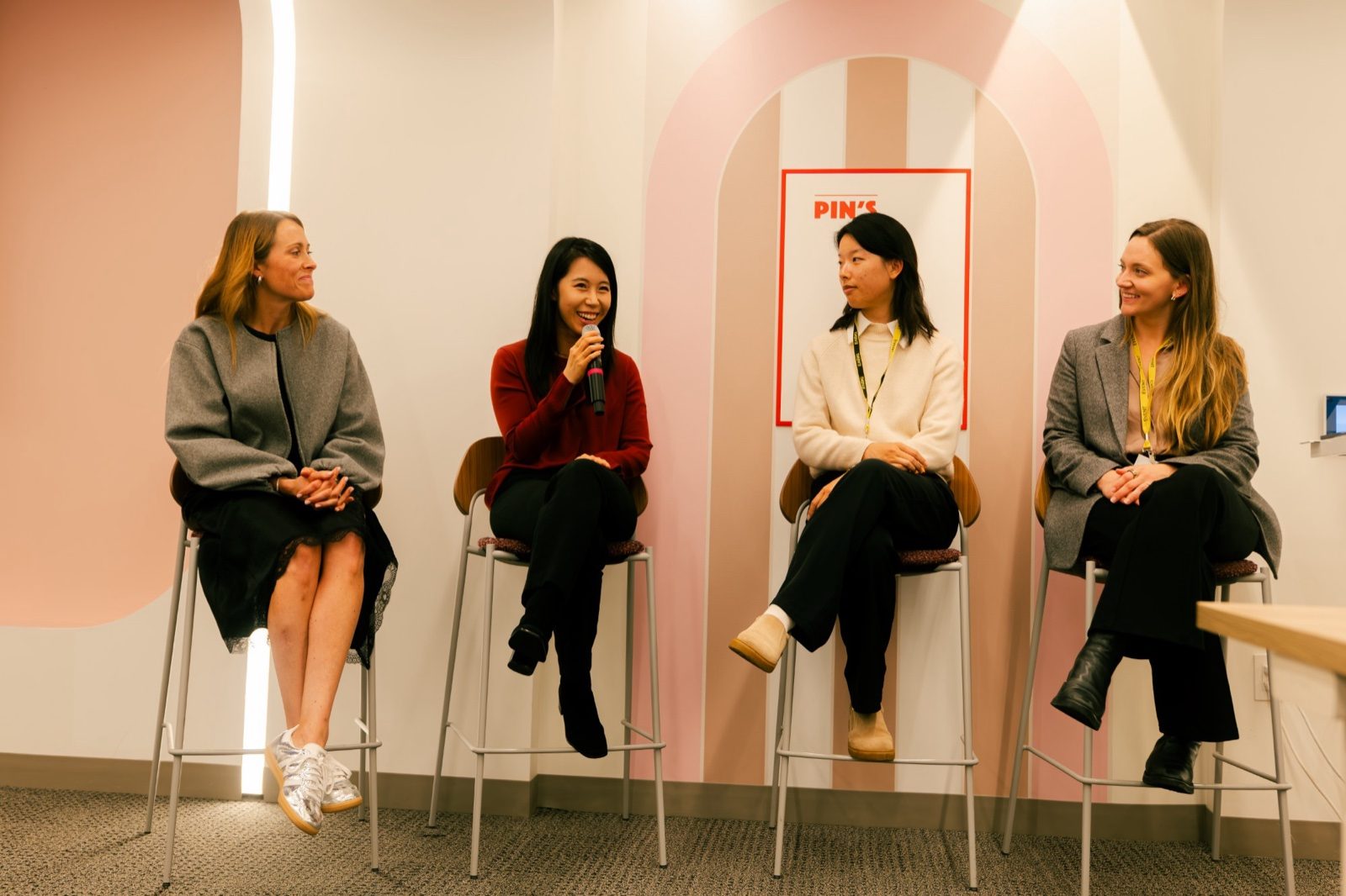 Four panelists on stools, one speaking into a microphone