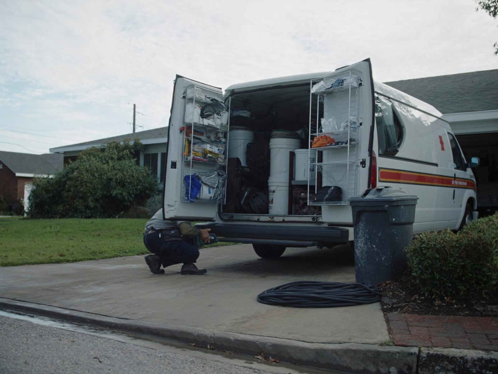 A service van backed into a residential driveway, rear doors open on organised tools and equipment